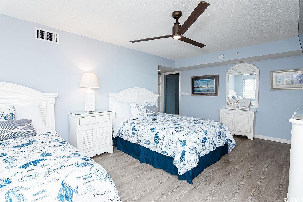 Bedroom with two beds in blue coastal-patterned bedding and a dark ceiling fan.