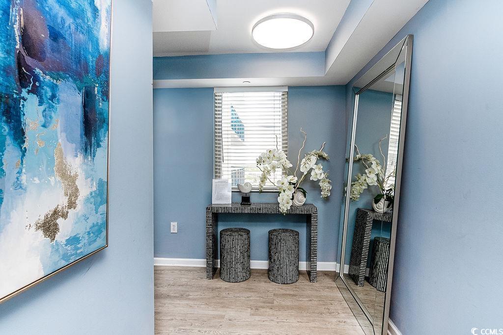 Blue entryway with a black console table, orchids, two stools, and a large leaning mirror.