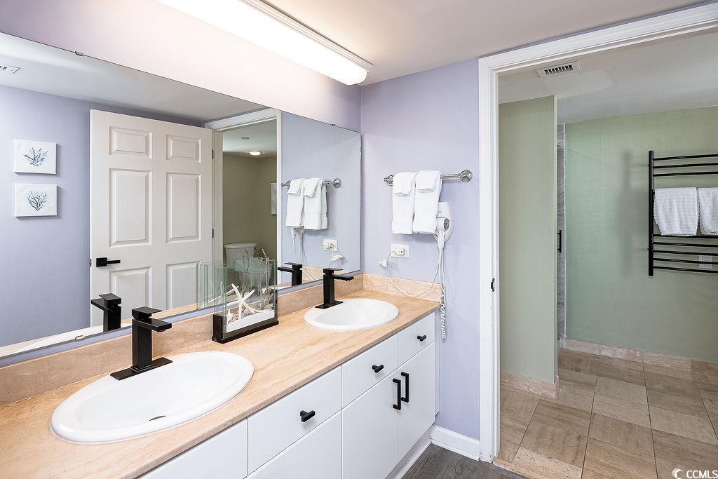 Bathroom with a double vanity and tan countertop, looking toward a tiled shower with a towel warmer.