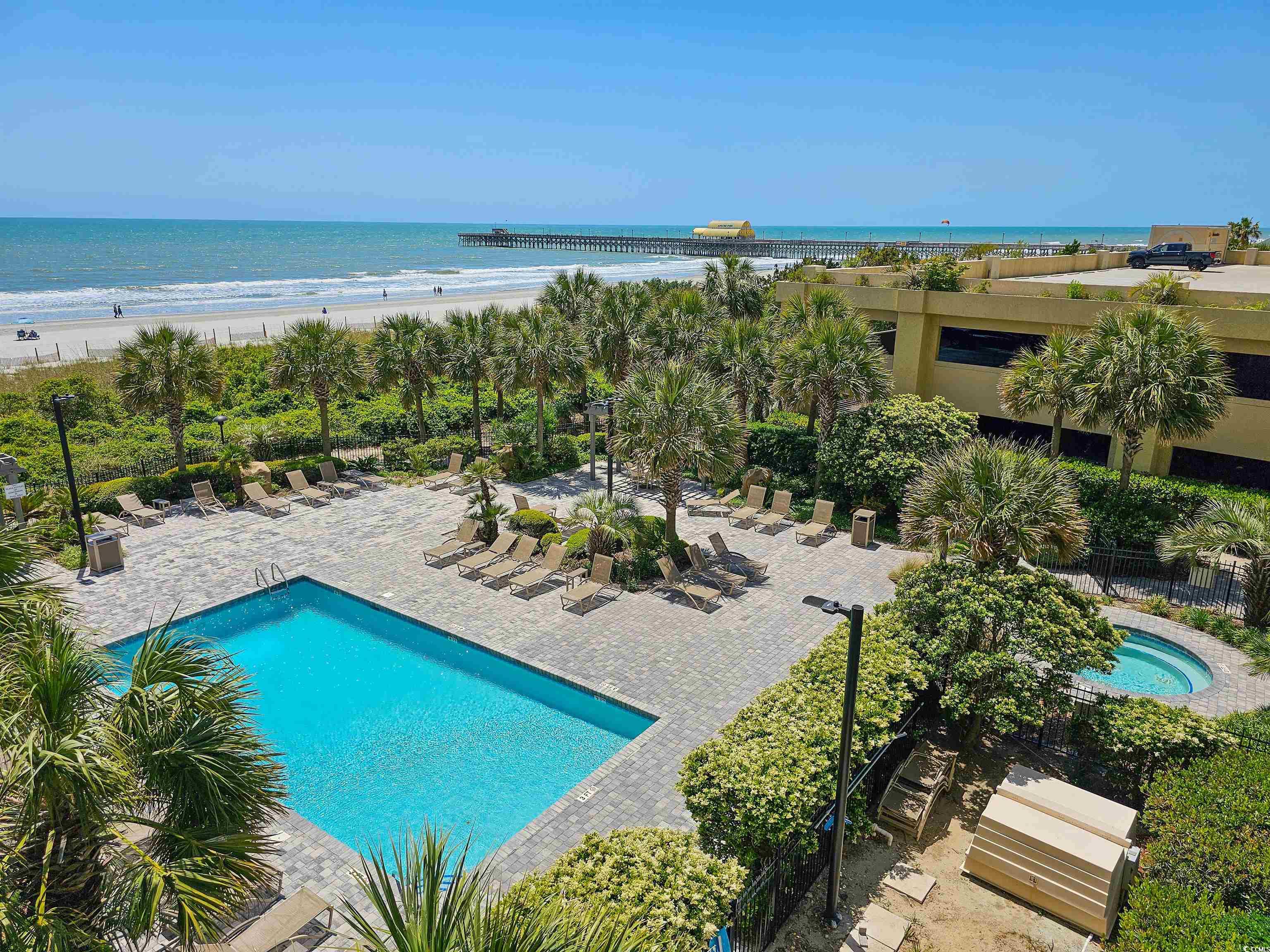 Outdoor pool and circular spa beside a palm-lined deck, with the beach, ocean, and pier beyond.