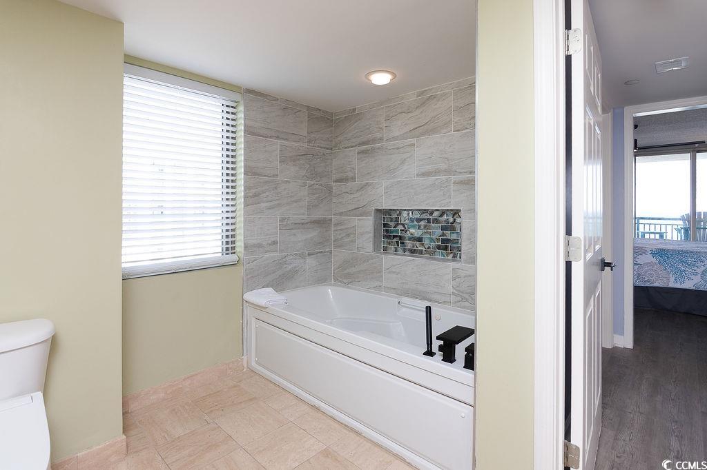 Bathroom with a white soaking tub, gray tile surround, and colorful mosaic shower niche.