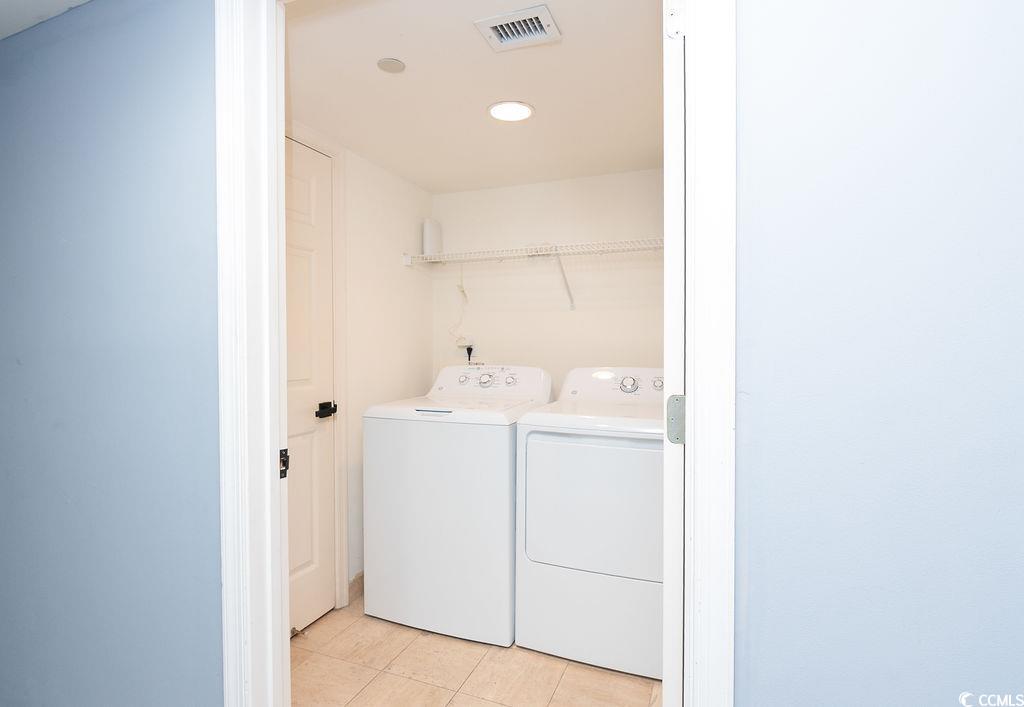 Laundry room with a white washer and dryer beneath a wire storage shelf.