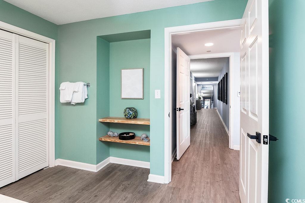 Mint-green room with louvered closet doors and wooden shelves opening onto a long hallway.