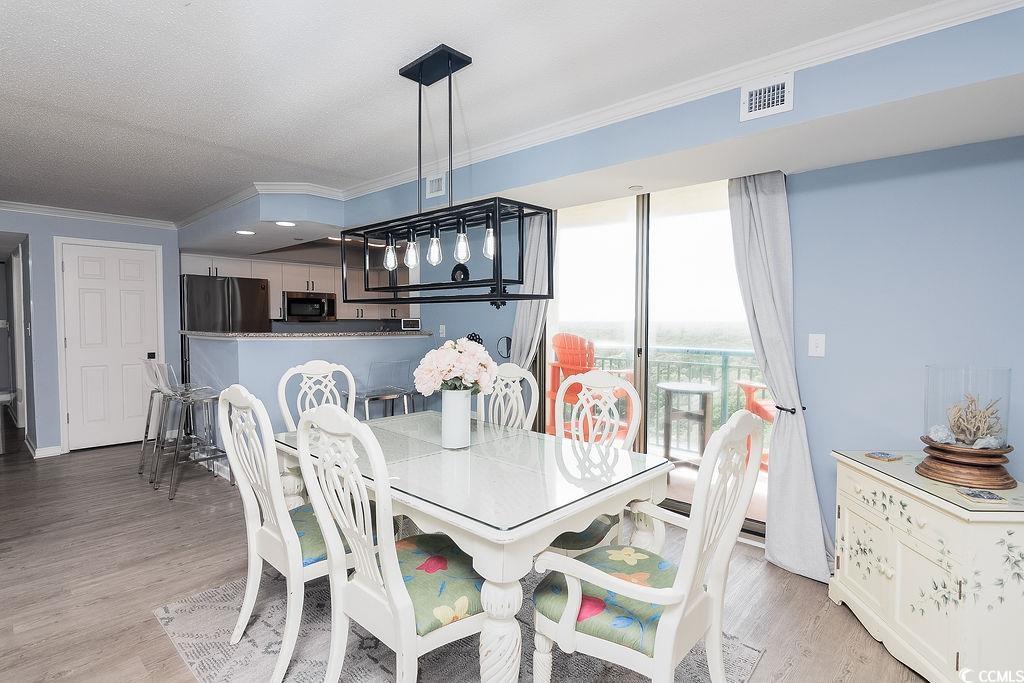Dining area with a glass-top table, white chairs, and balcony doors beside the open kitchen.