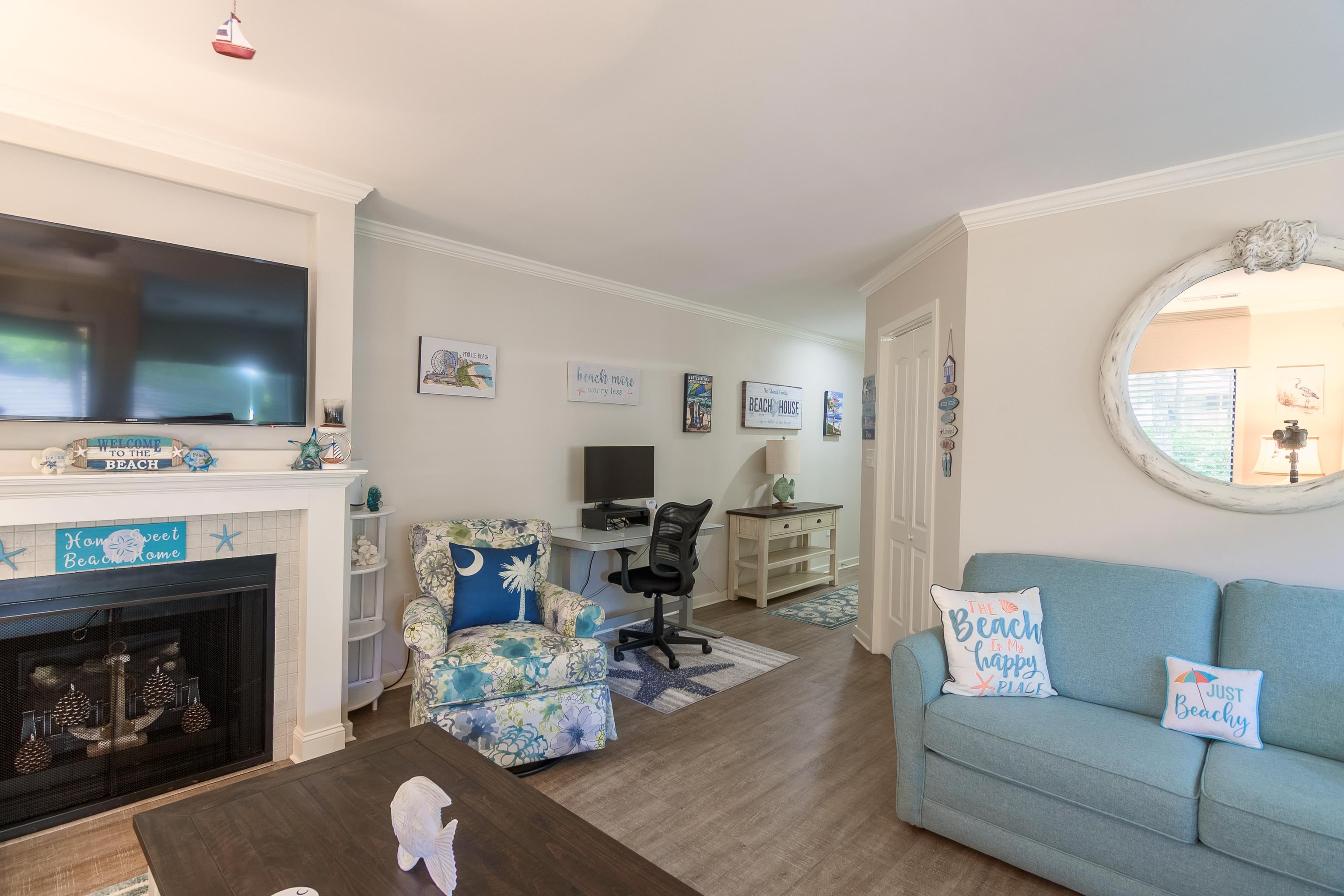 Furnished living room with a fireplace, blue sofa, floral armchair, and desk.