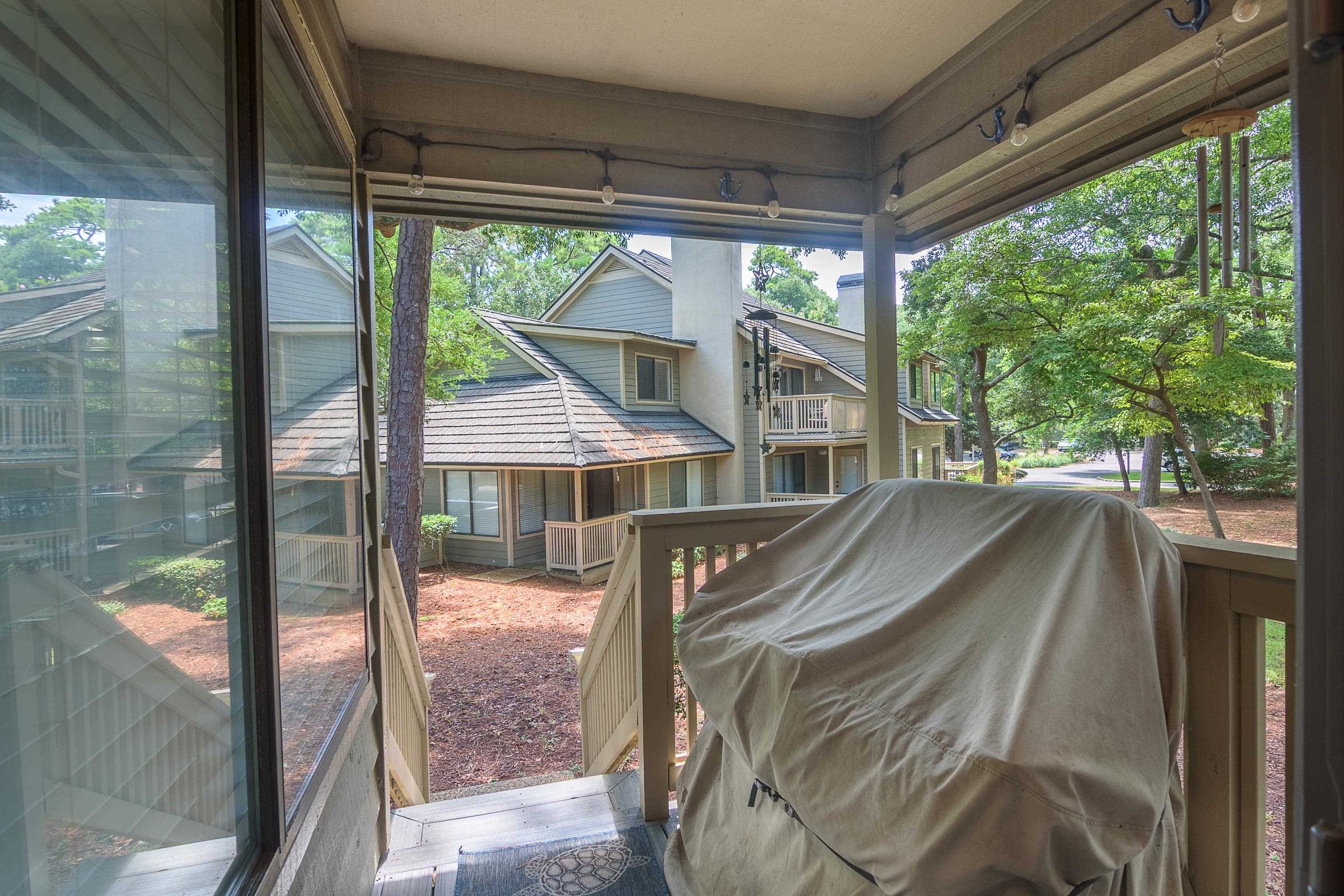 Covered townhouse patio with a covered grill, overlooking neighboring homes and leafy trees.