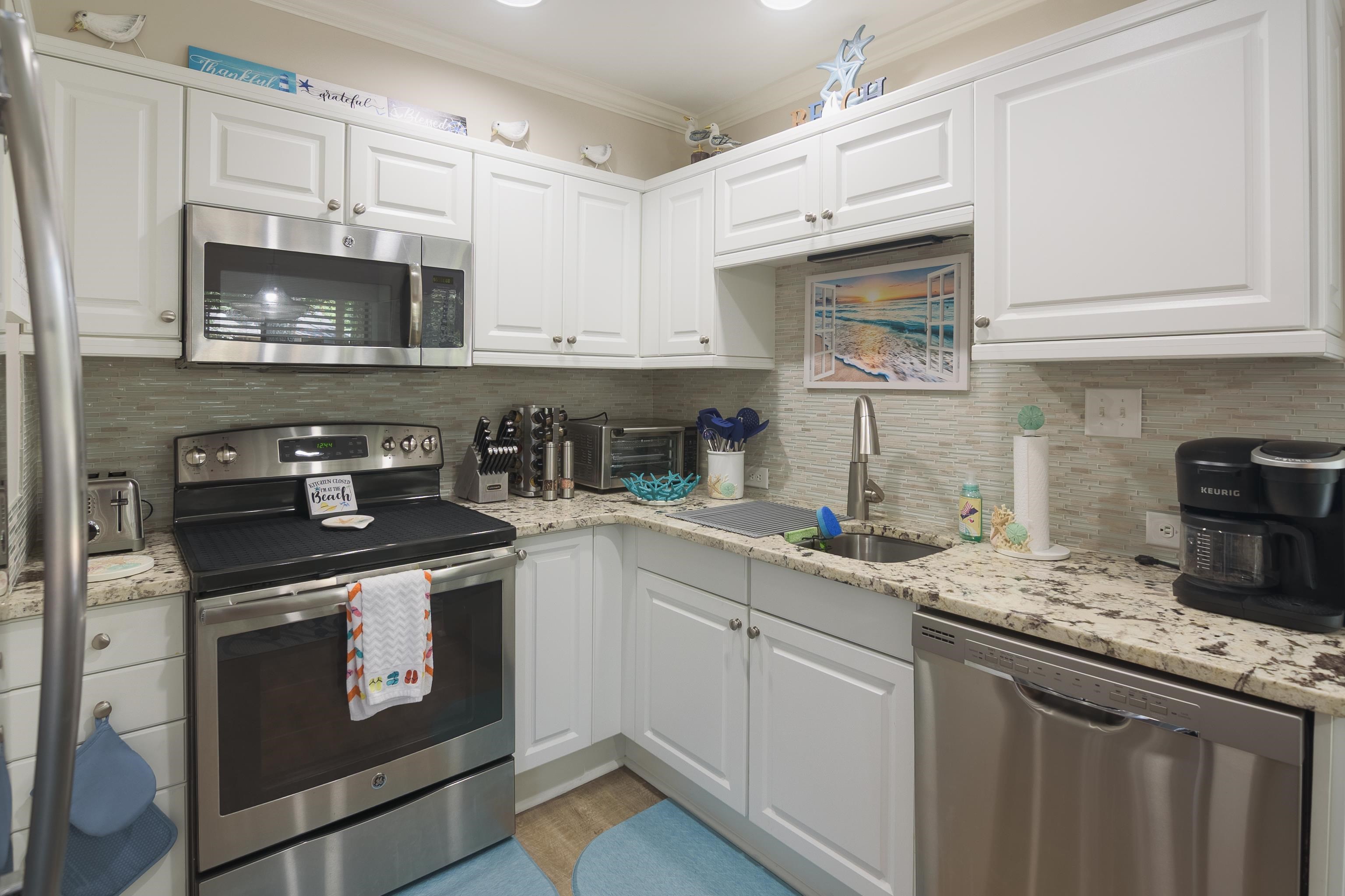 Bright kitchen with white cabinets, stainless steel appliances, granite counters, and a framed beach scene.