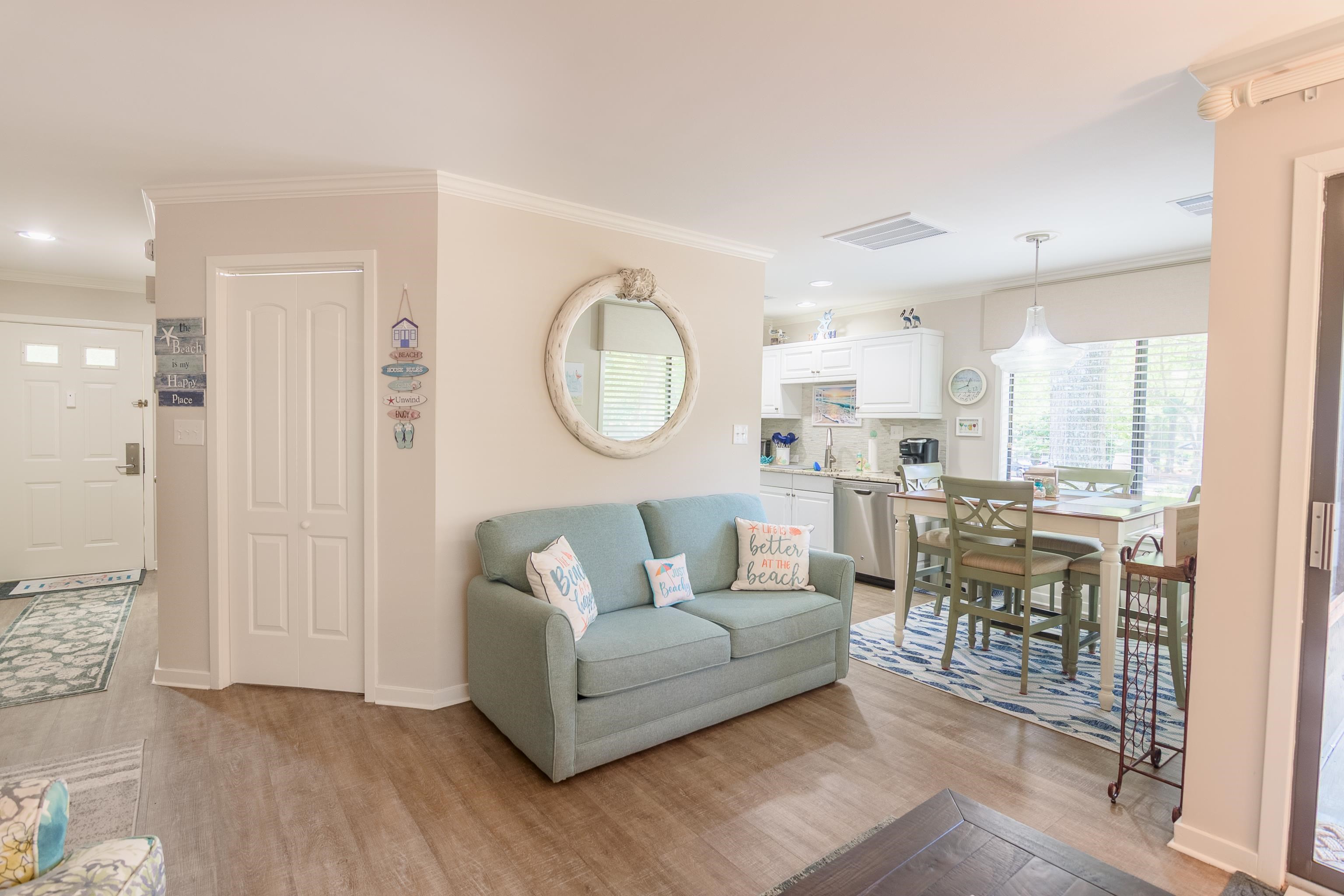 Furnished living room with a gray sofa opening to a white kitchen and dining area.