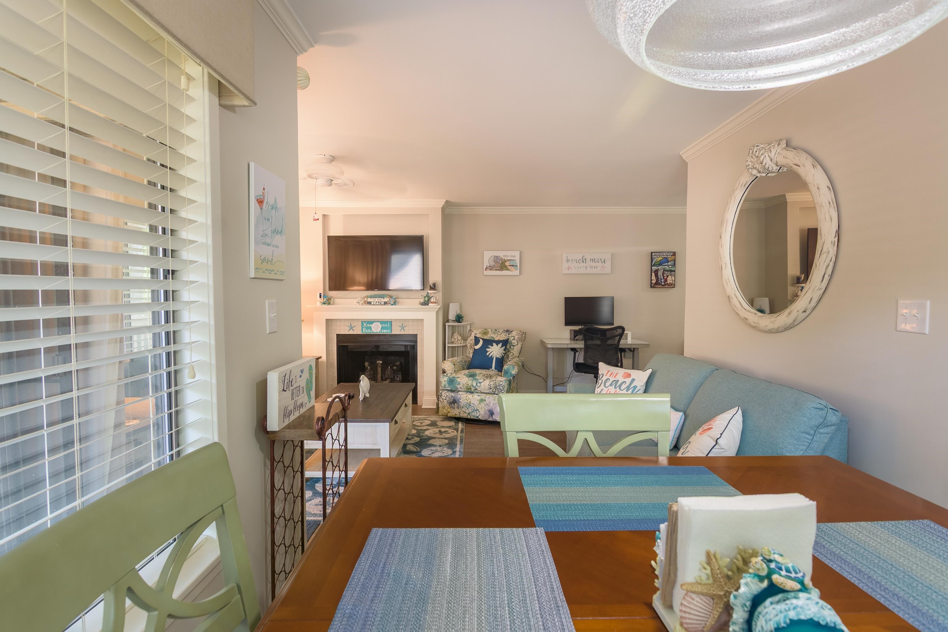 Furnished living and dining room with a tiled fireplace, blue sofa, and beach-themed decor.
