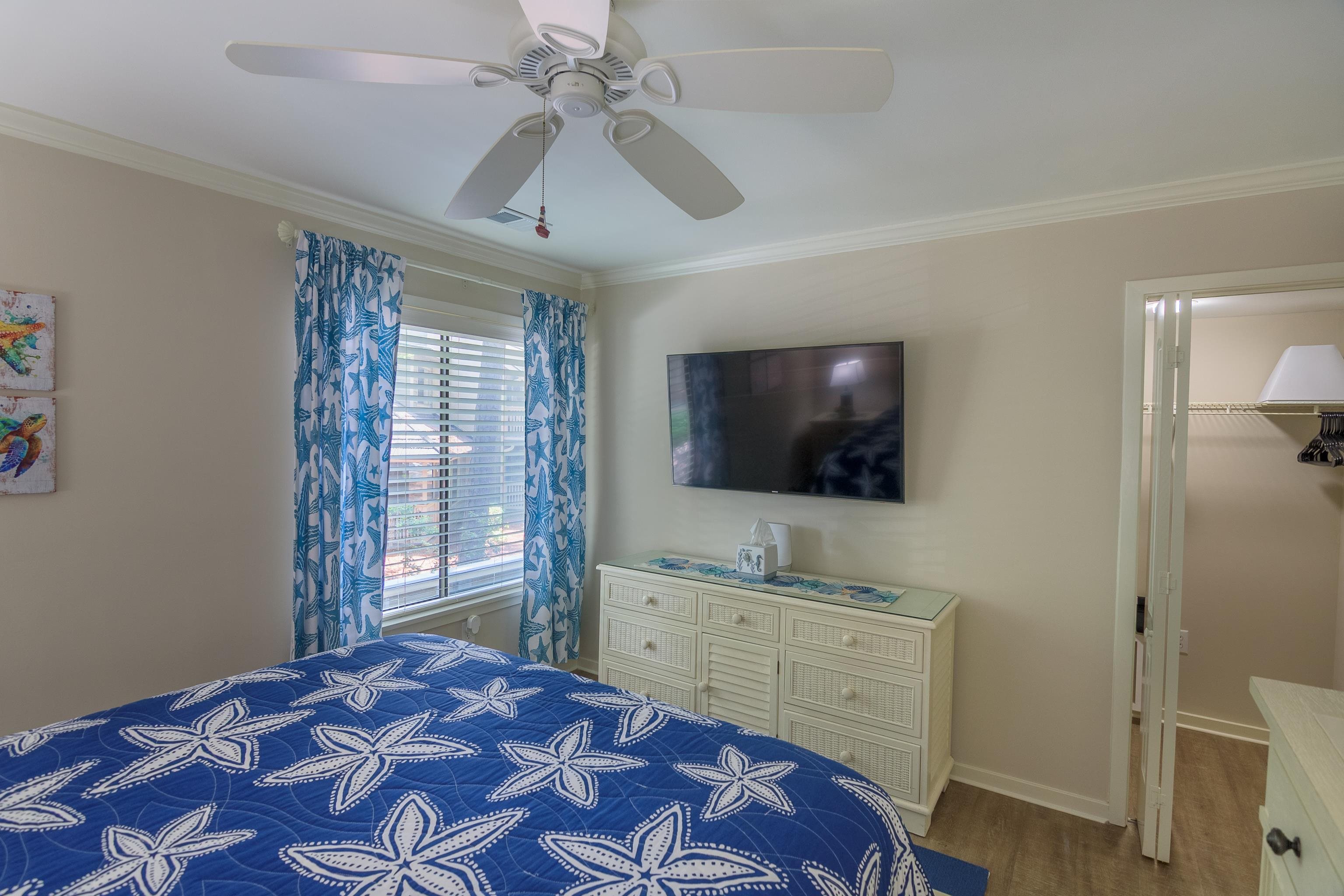 Bedroom with blue starfish-patterned bedding, a ceiling fan, and a dresser beneath a wall-mounted TV.