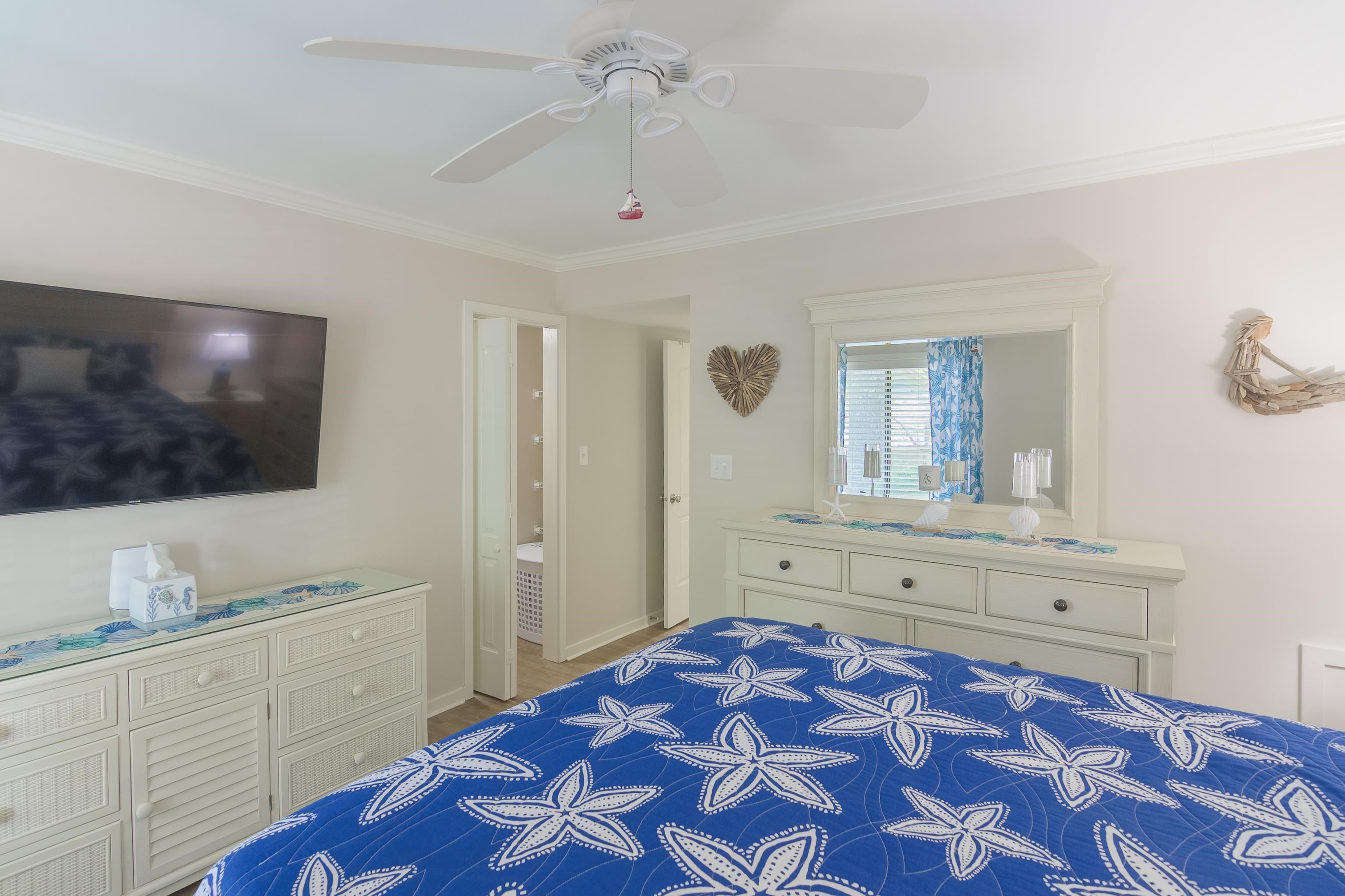 Bedroom with a blue starfish-patterned bedspread, white dresser, and ceiling fan.