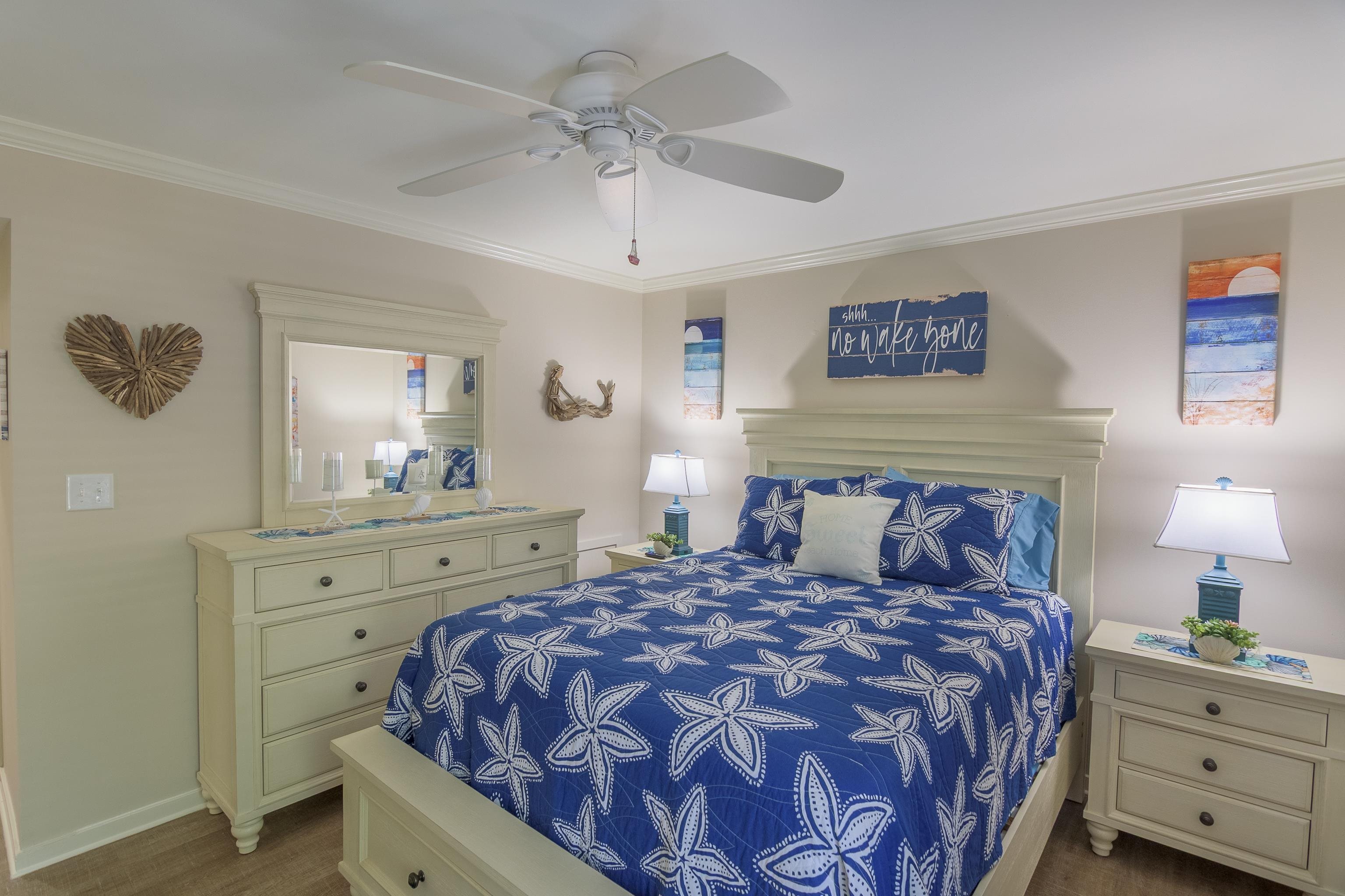 Bedroom with blue starfish-patterned bedding, pale wood furniture, and coastal wall decor.