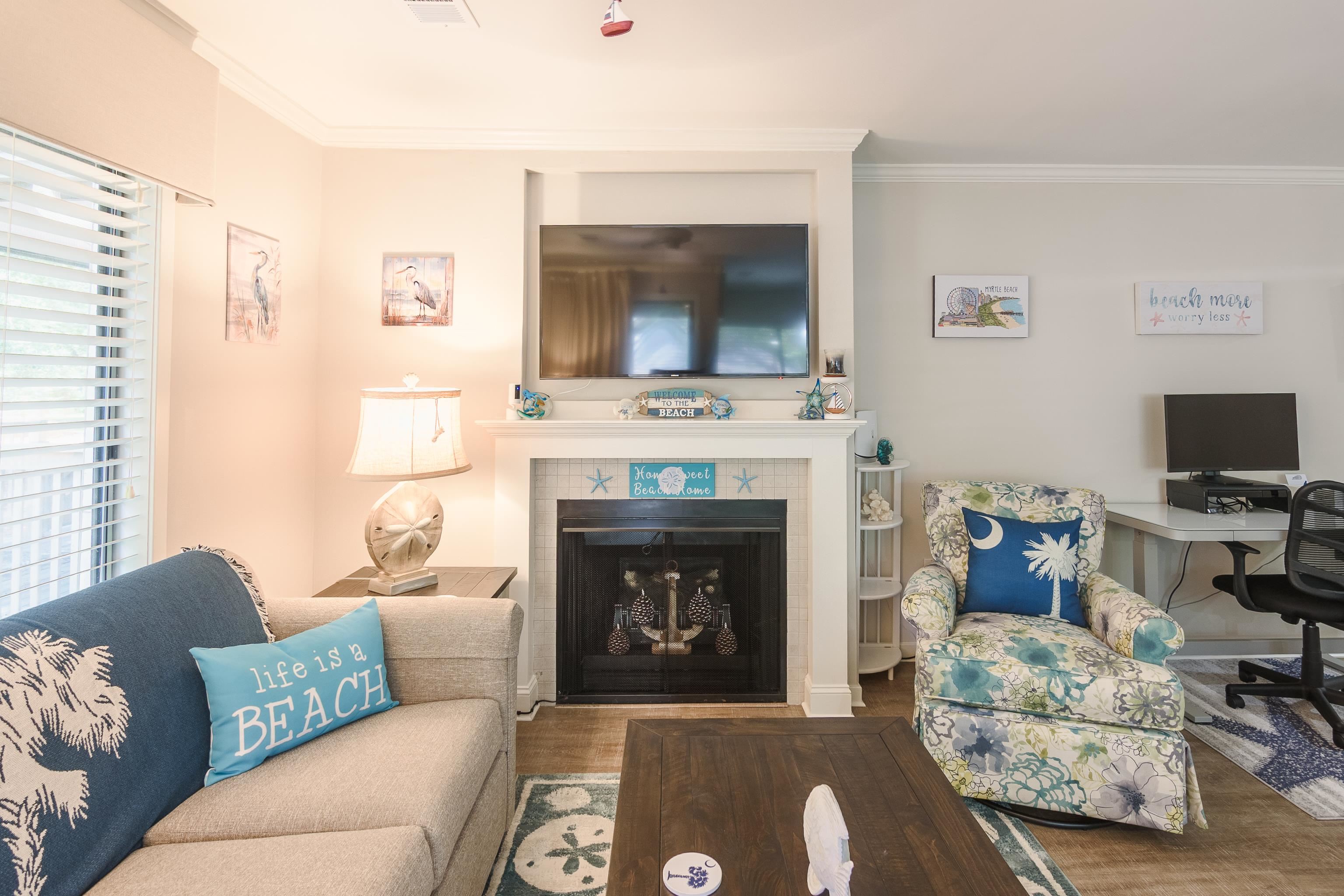 Beach-themed living room with a fireplace, television, floral armchair, and desk.