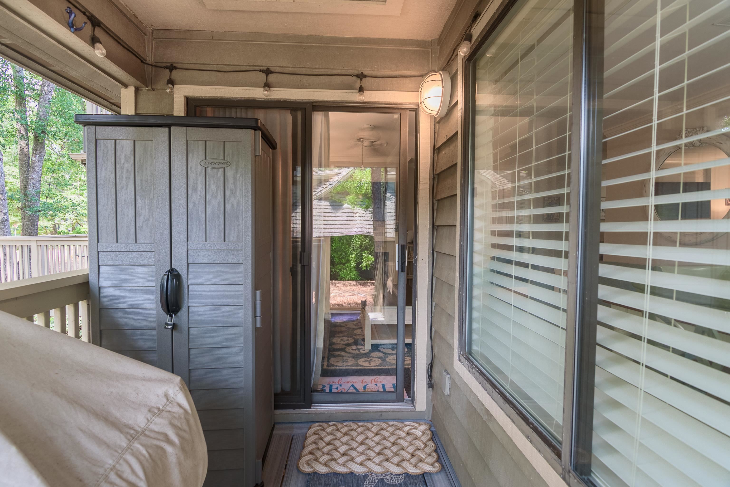 Covered condo entry porch with a gray storage cabinet, rope mat, and sliding glass door.