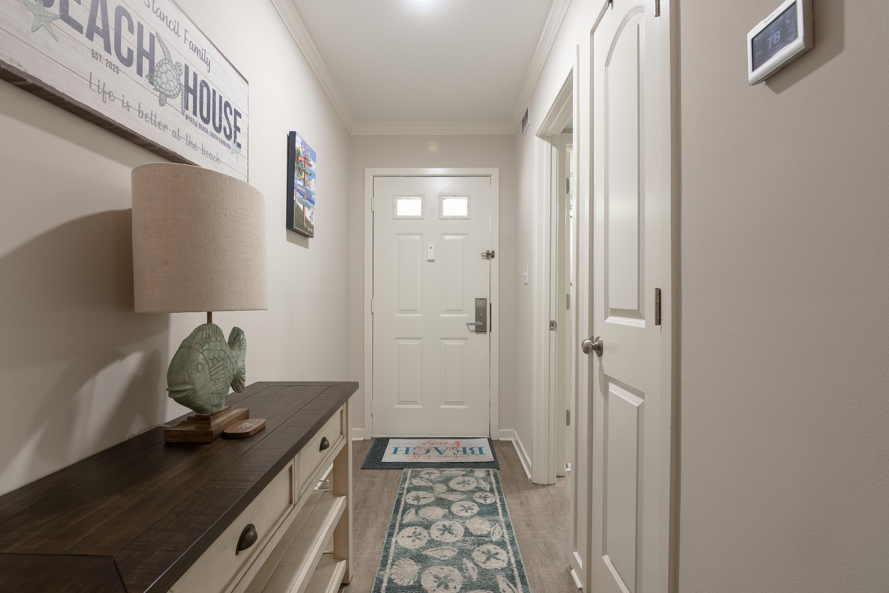 Entry hallway with a dark console, fish-shaped lamp, patterned runner, and white front door.