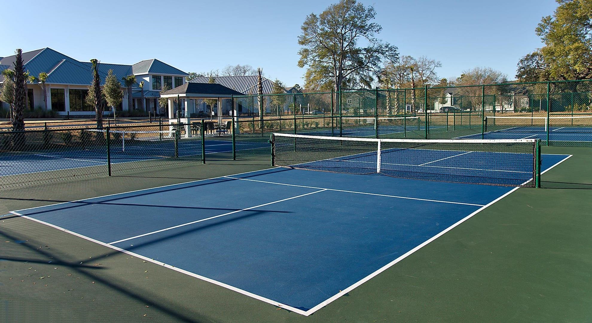Blue tennis courts with chain-link fencing, nets, and a covered seating pavilion.