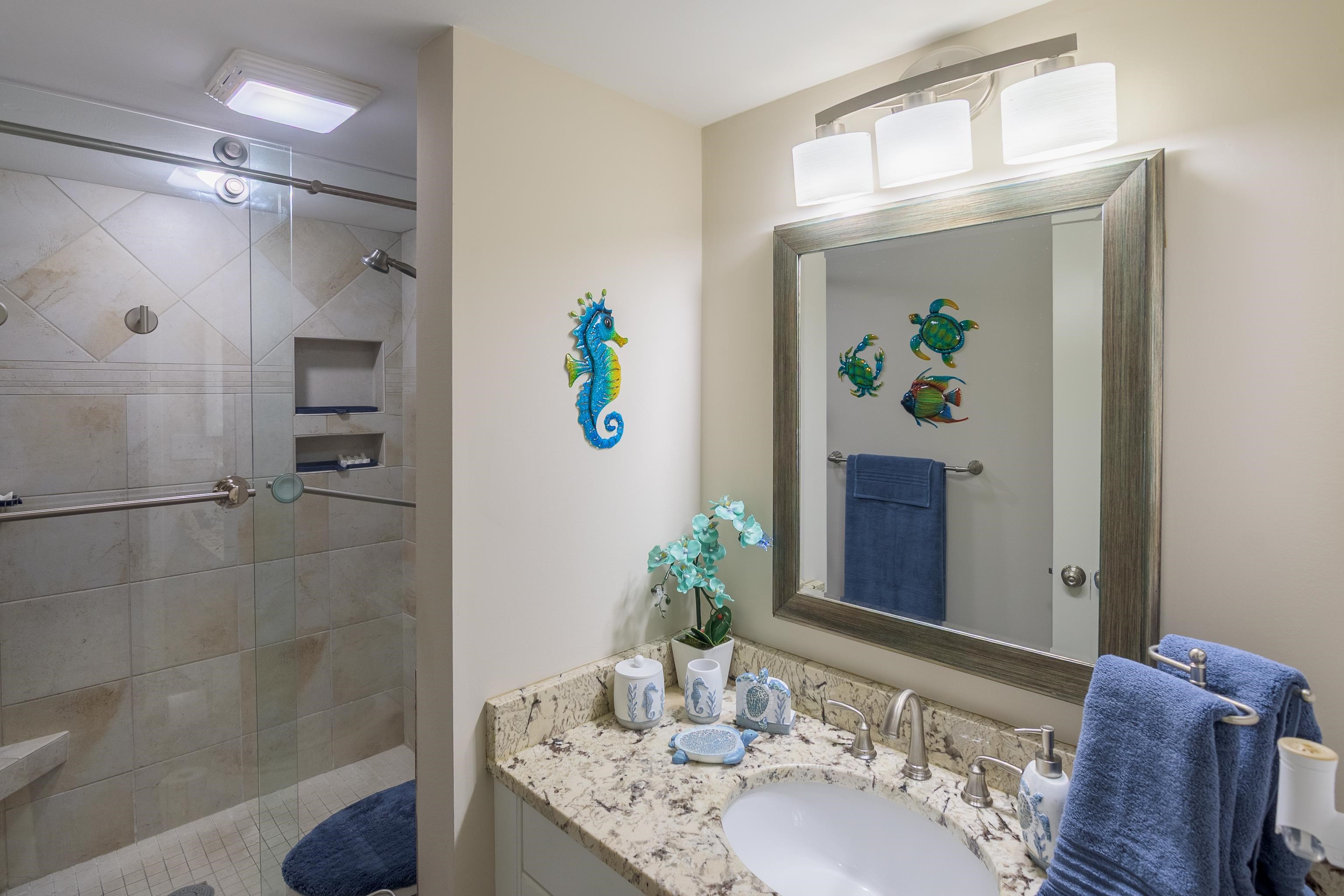 Bathroom with a glass-enclosed tiled shower and granite vanity decorated with coastal accents.