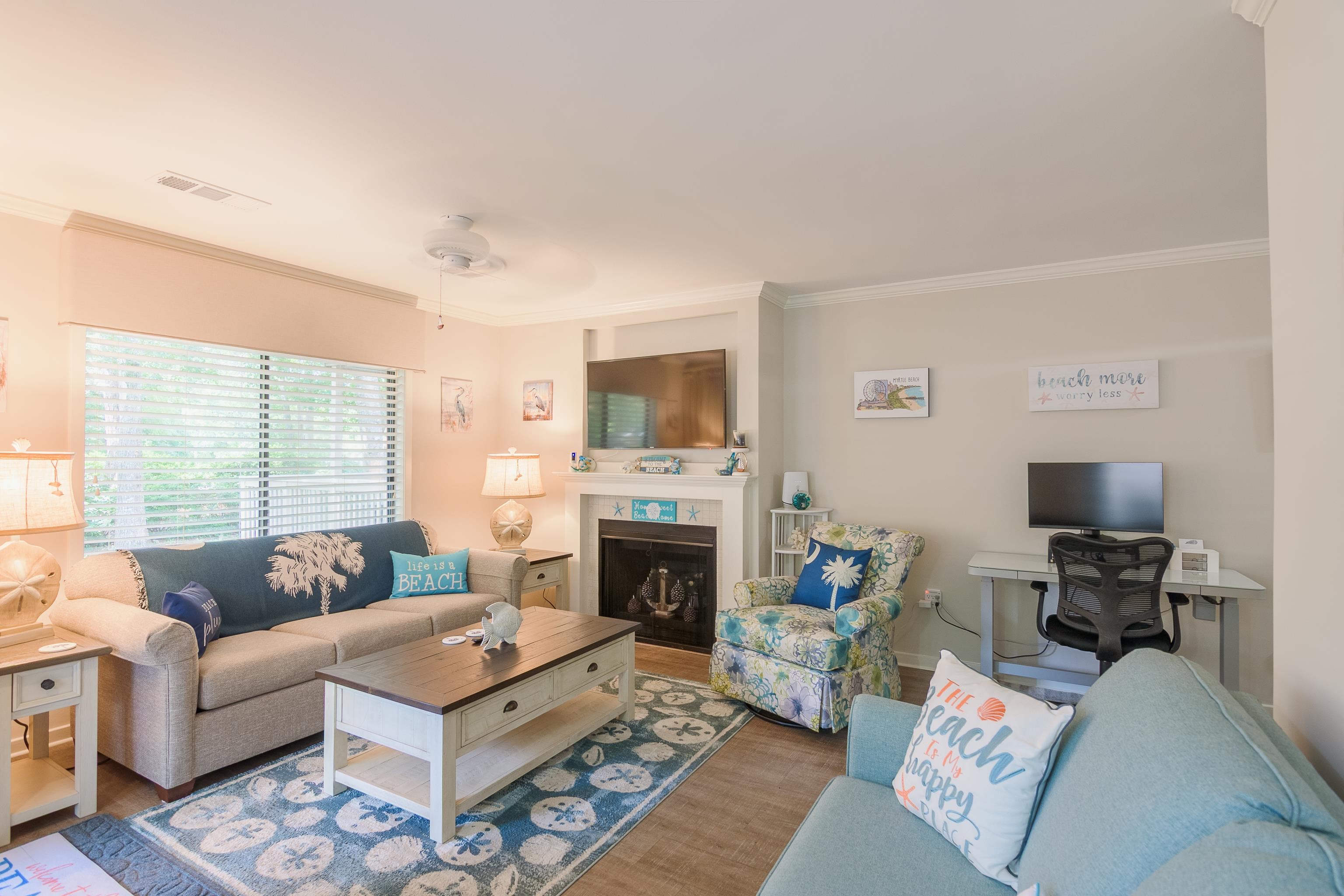 Furnished living room with a fireplace, blue sofas, patterned rug, and beach-themed decor.