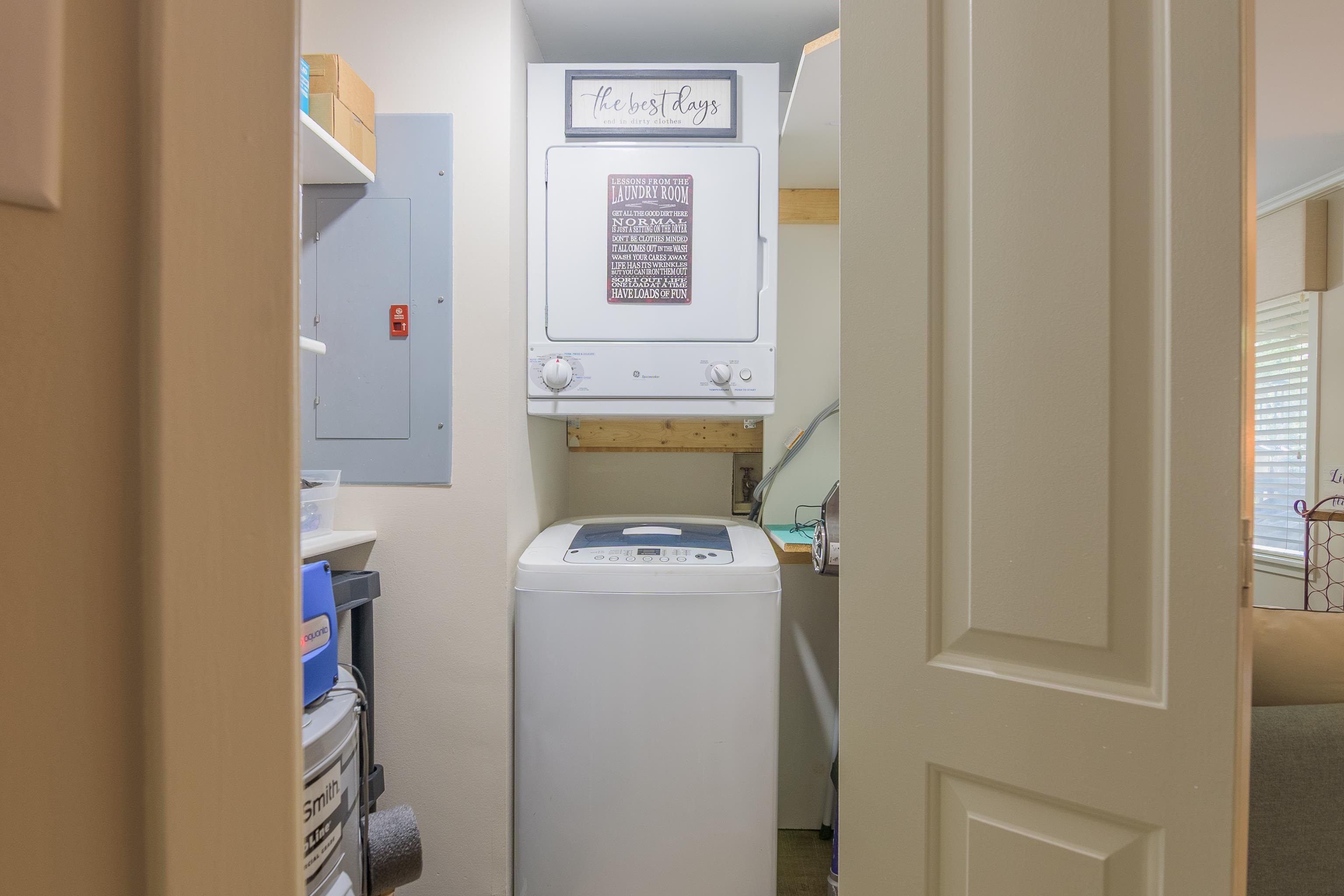 Laundry room with a top-load washer beneath a wall-mounted dryer and laundry-themed signs.