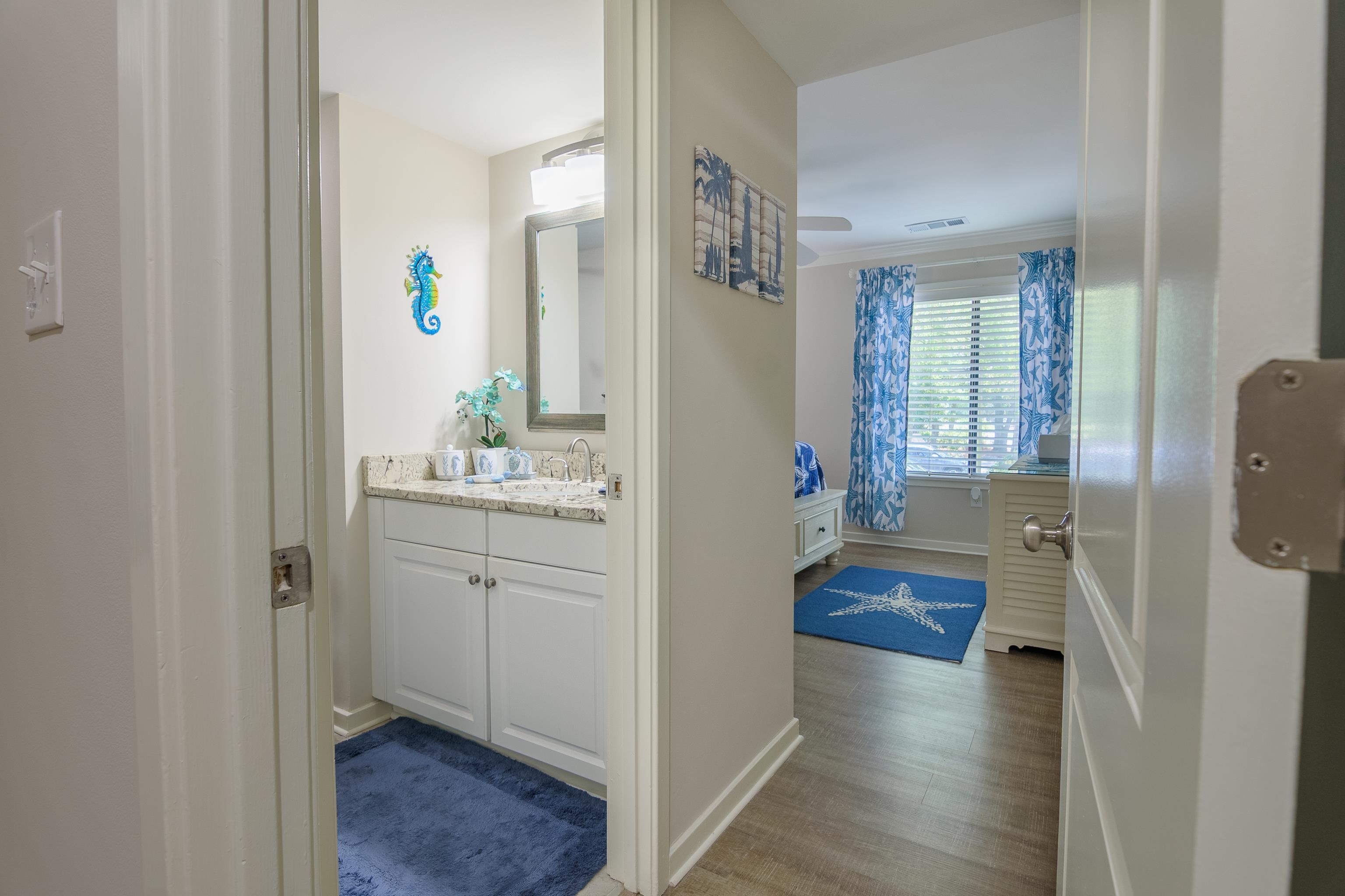 Bathroom vanity and blue coastal-themed bedroom viewed through an open hallway.