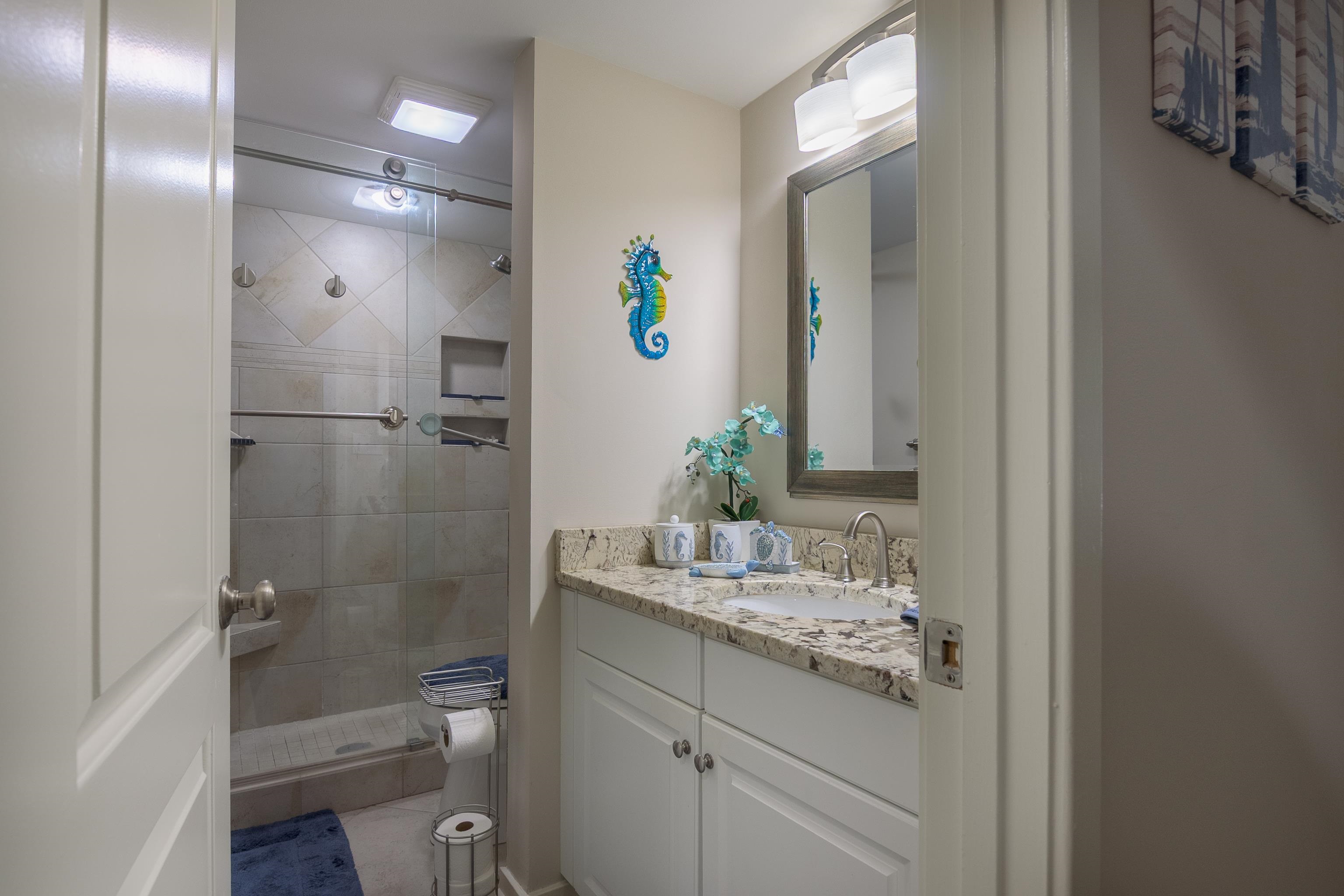 Bathroom with a tiled glass shower, granite vanity, and blue seahorse wall decoration.