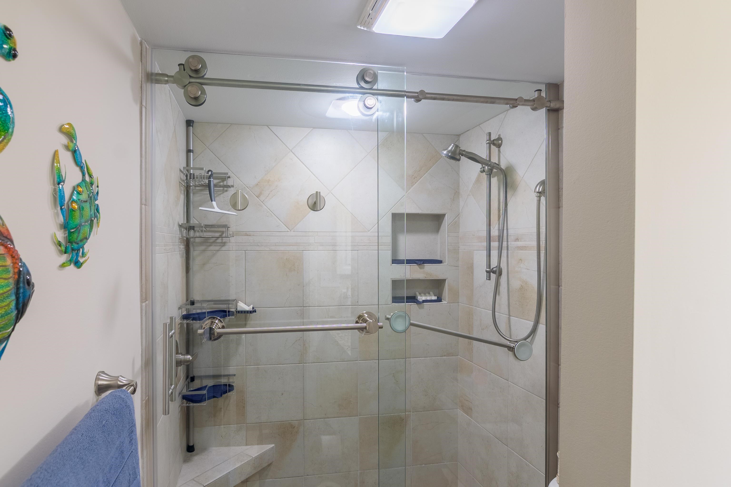 Walk-in shower with beige tile, glass enclosure, grab bars, and recessed shelves.