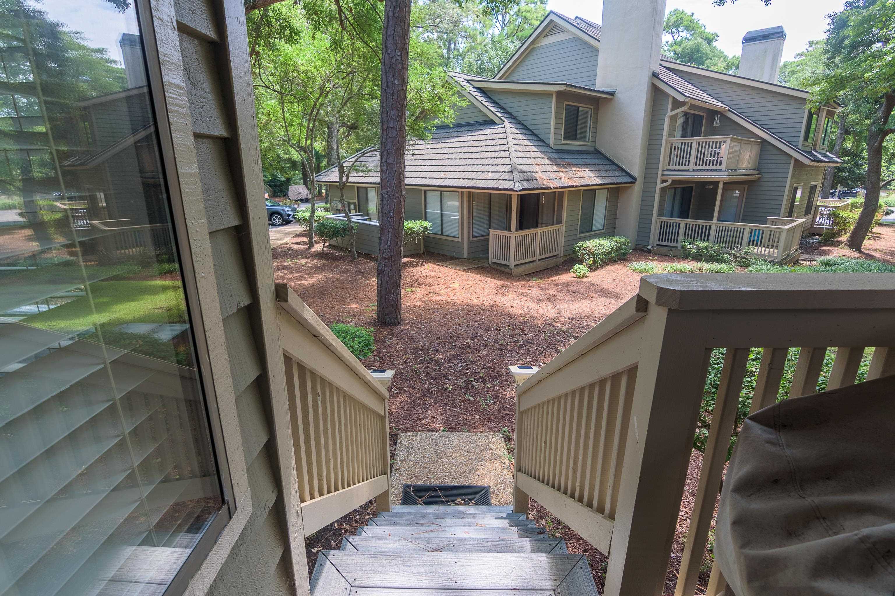 Wooden deck stairs overlook a landscaped courtyard and neighboring condos among mature trees.