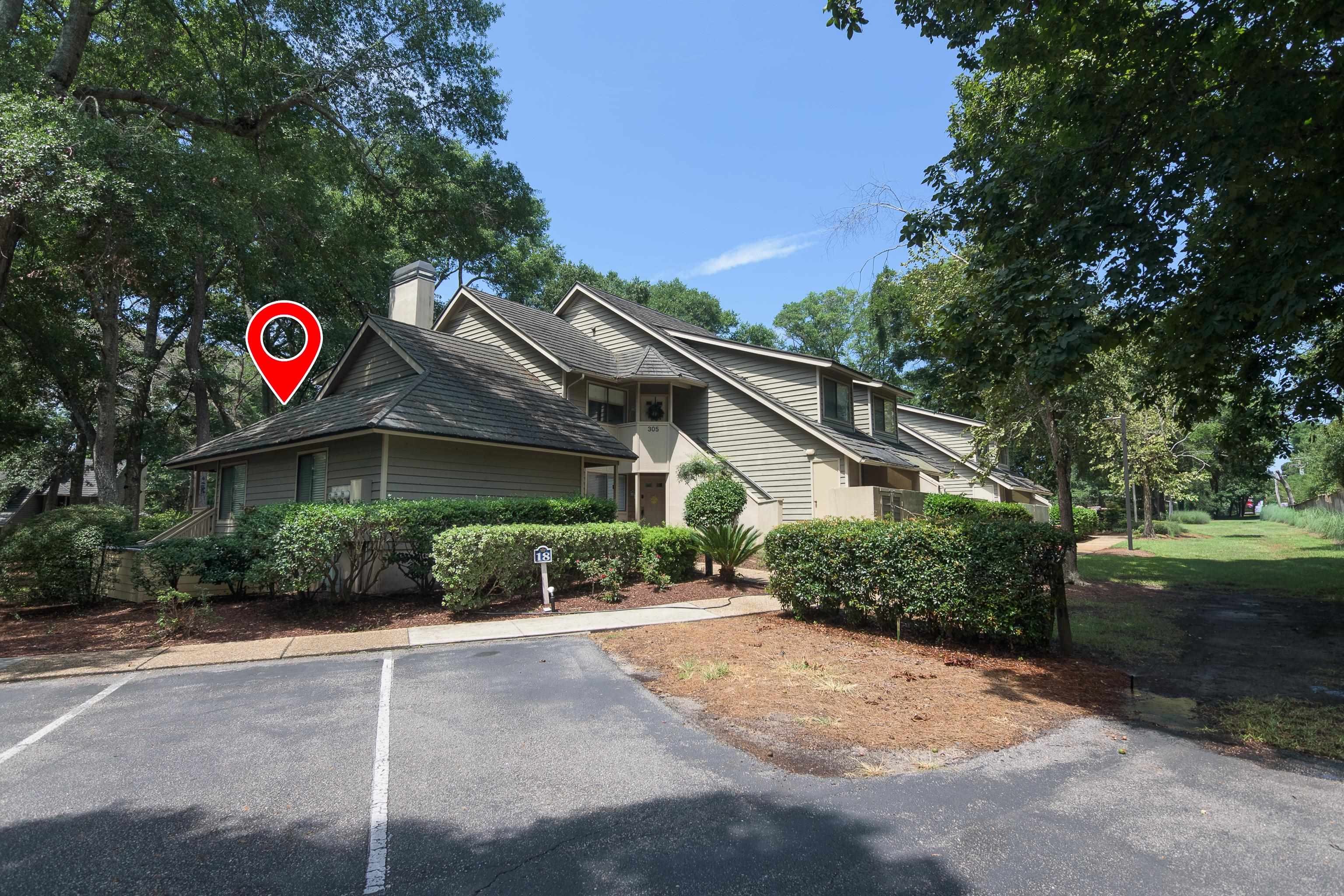 Condominium exterior with gabled roofs, mature trees, and a red location marker.