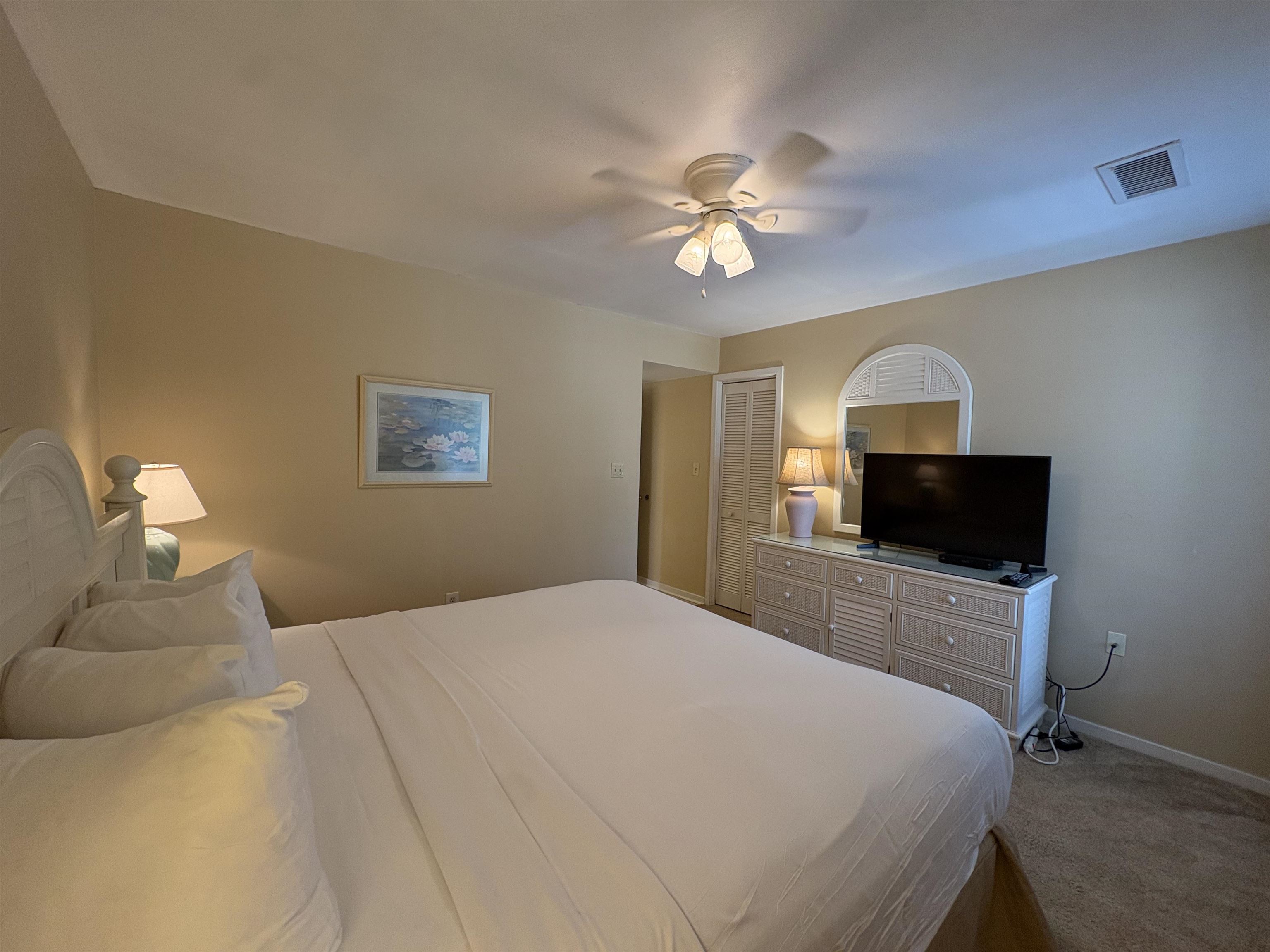 Bedroom with a large white bed, ceiling fan, and TV on a dresser.