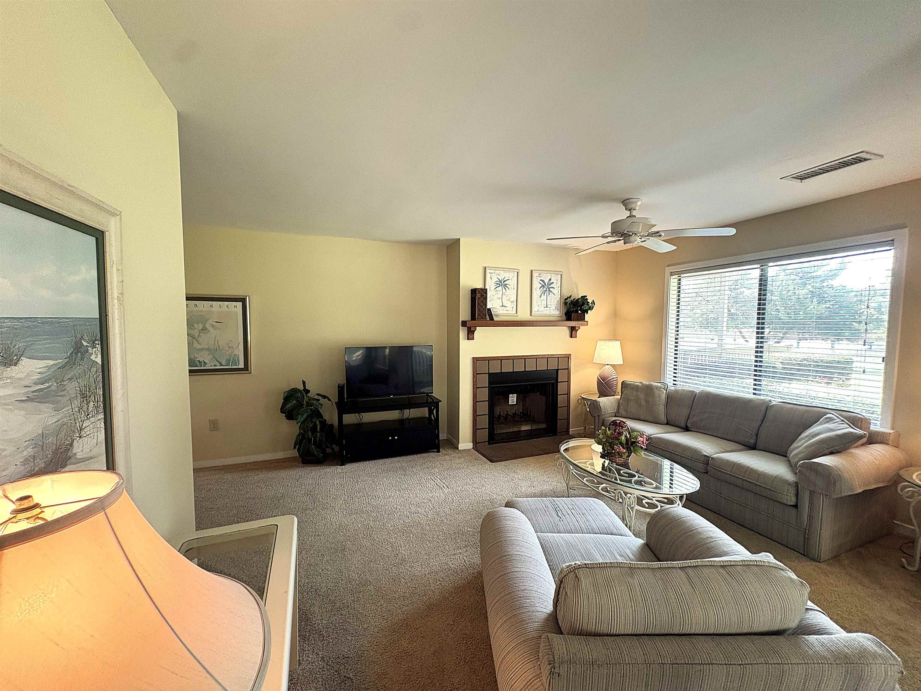 Living room with a tiled fireplace, gray sofas, and a bright window with blinds.