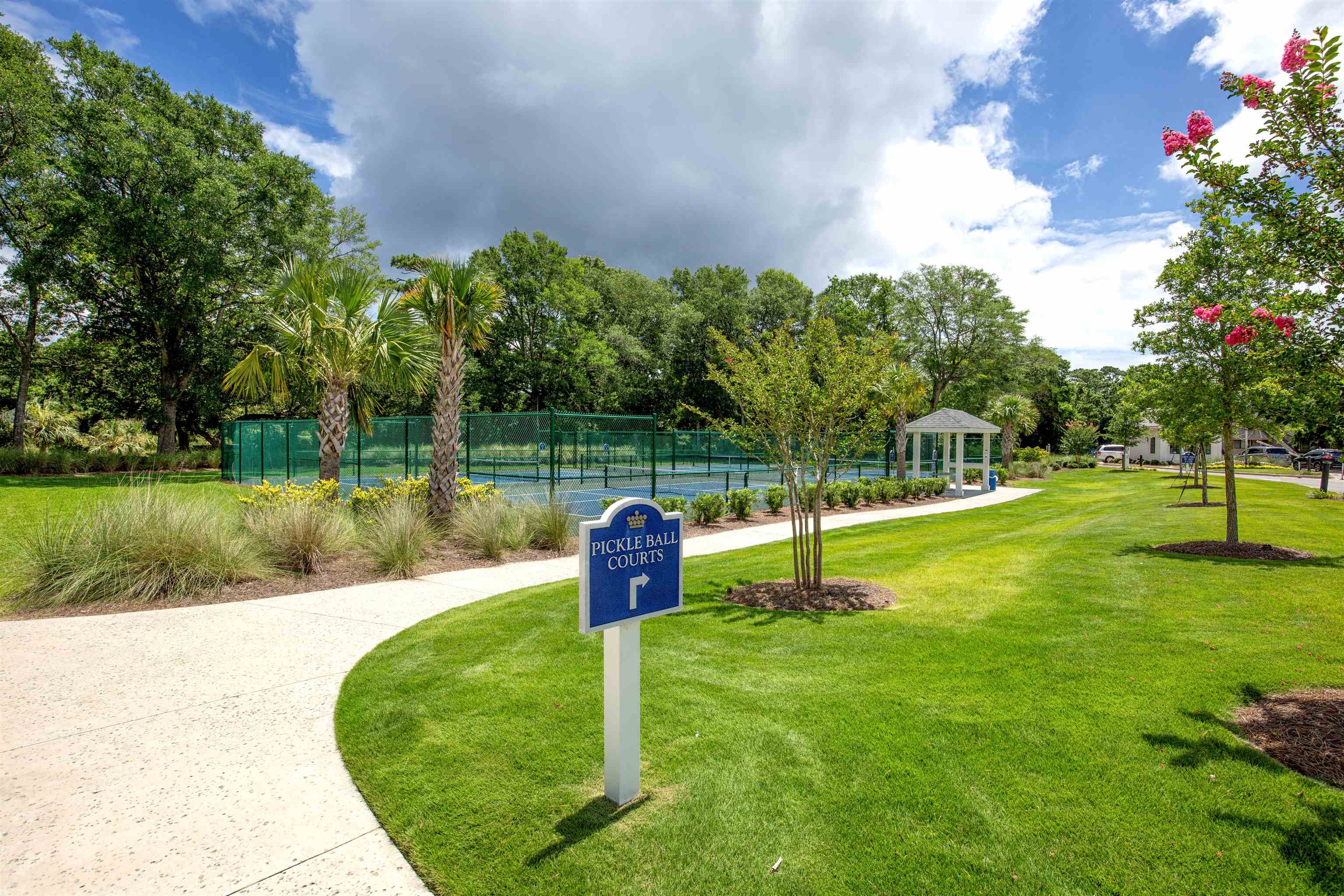 Community pickleball courts beside a landscaped lawn, marked by a blue directional sign.