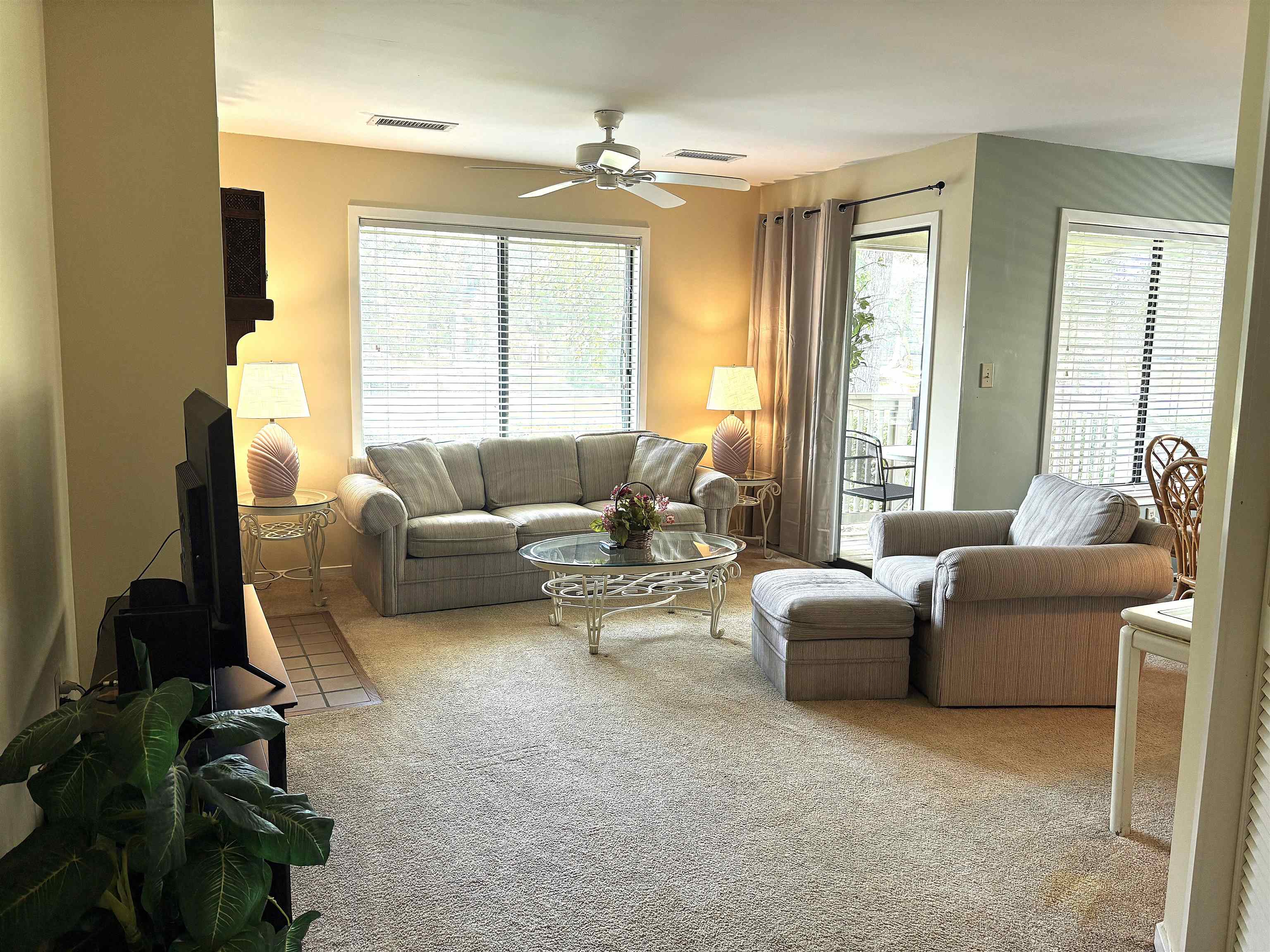 Furnished living room with gray seating, a glass coffee table, and windows opening to a balcony.