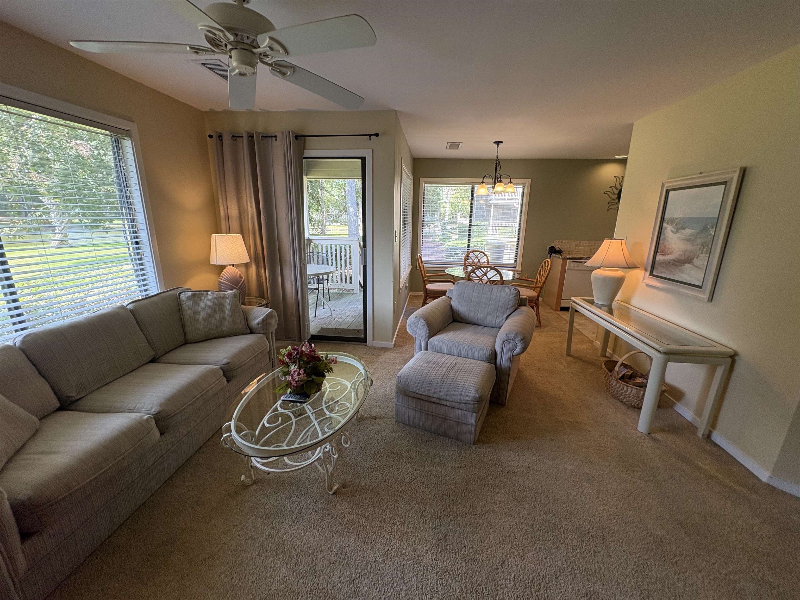 Furnished living room with a gray sofa, glass coffee table, and dining area beside a balcony door.