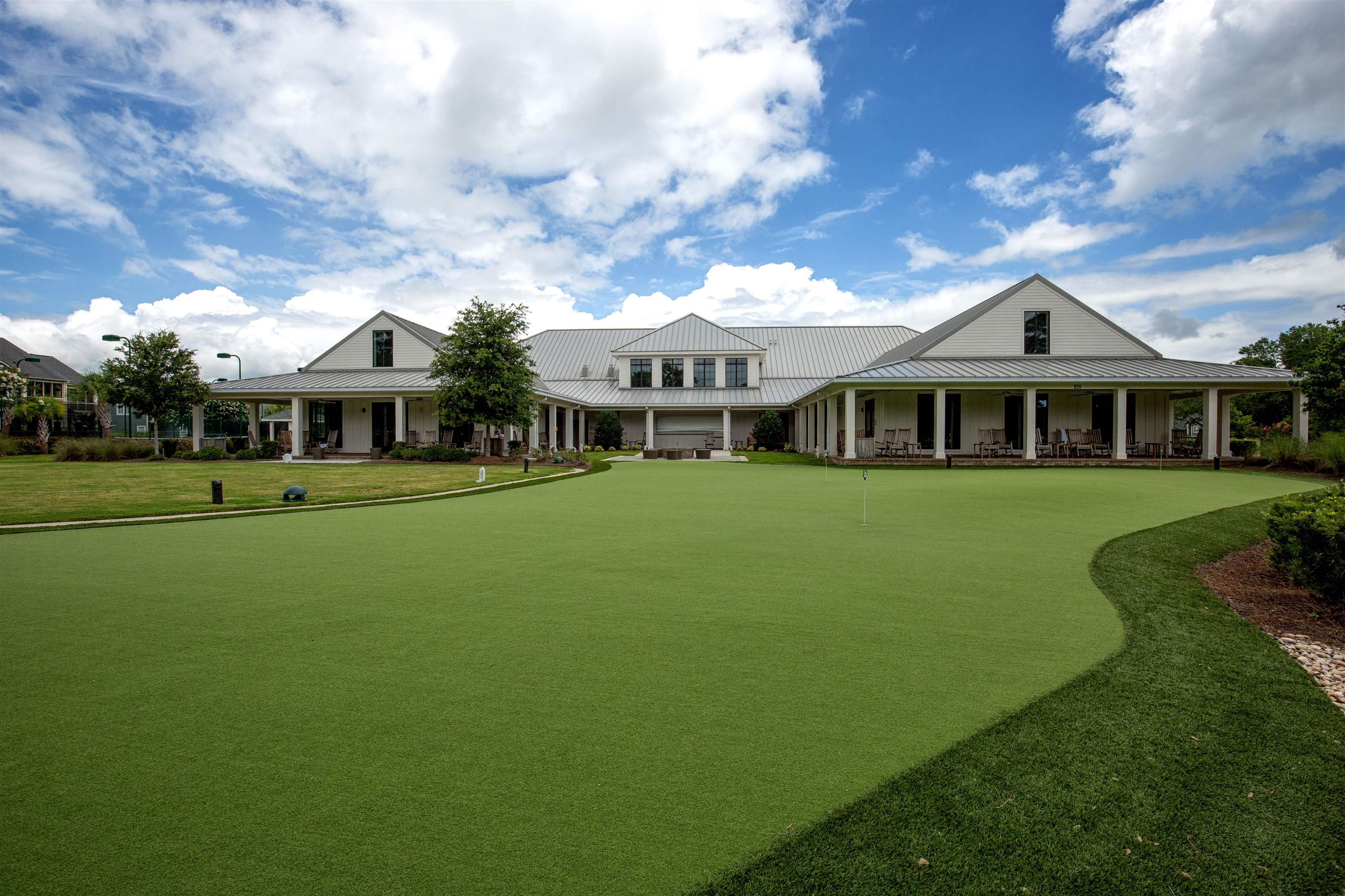 Community clubhouse beside a broad putting green, with covered patios and seating.