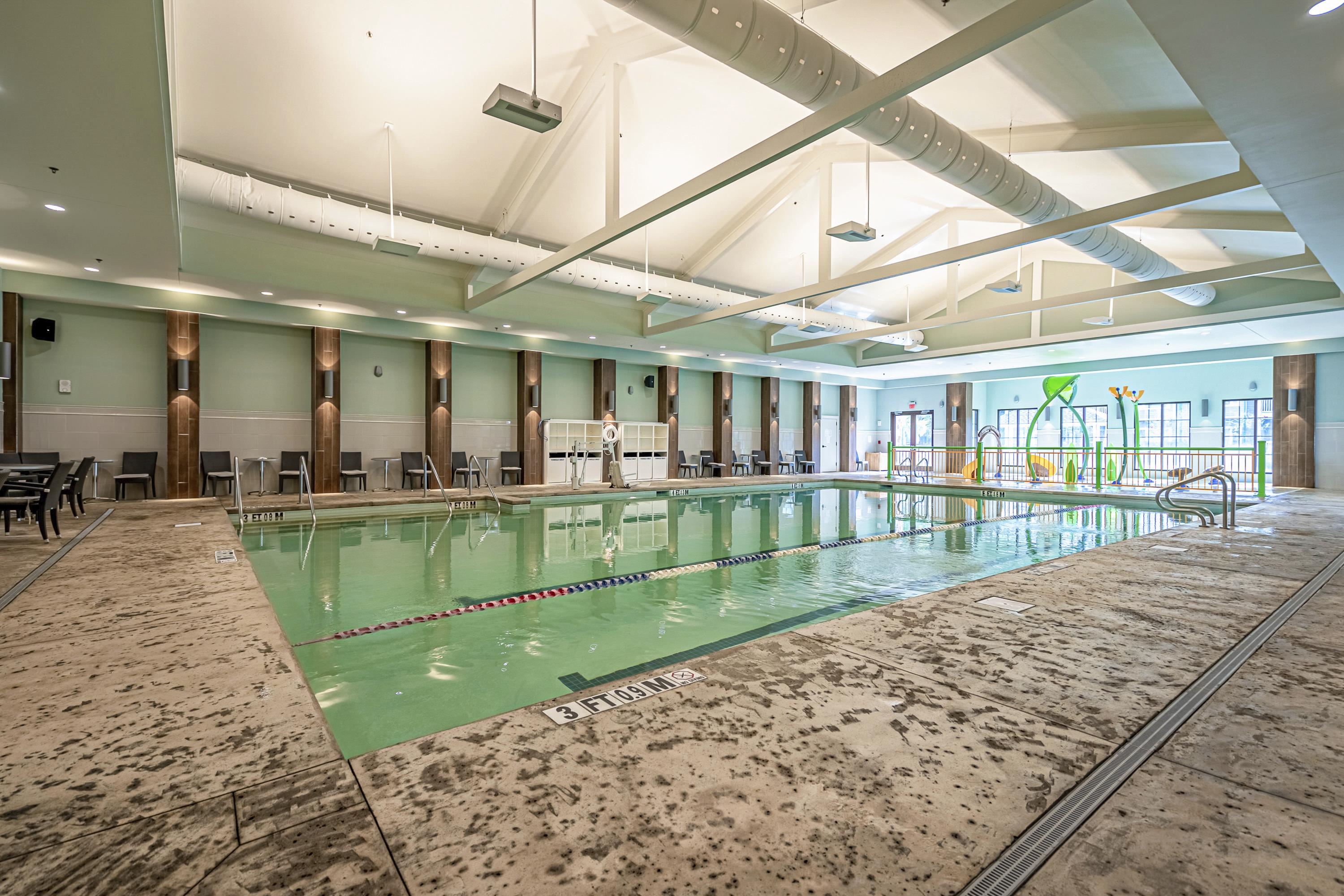 Indoor swimming pool with lane divider, surrounding seating, and colorful water-play features.
