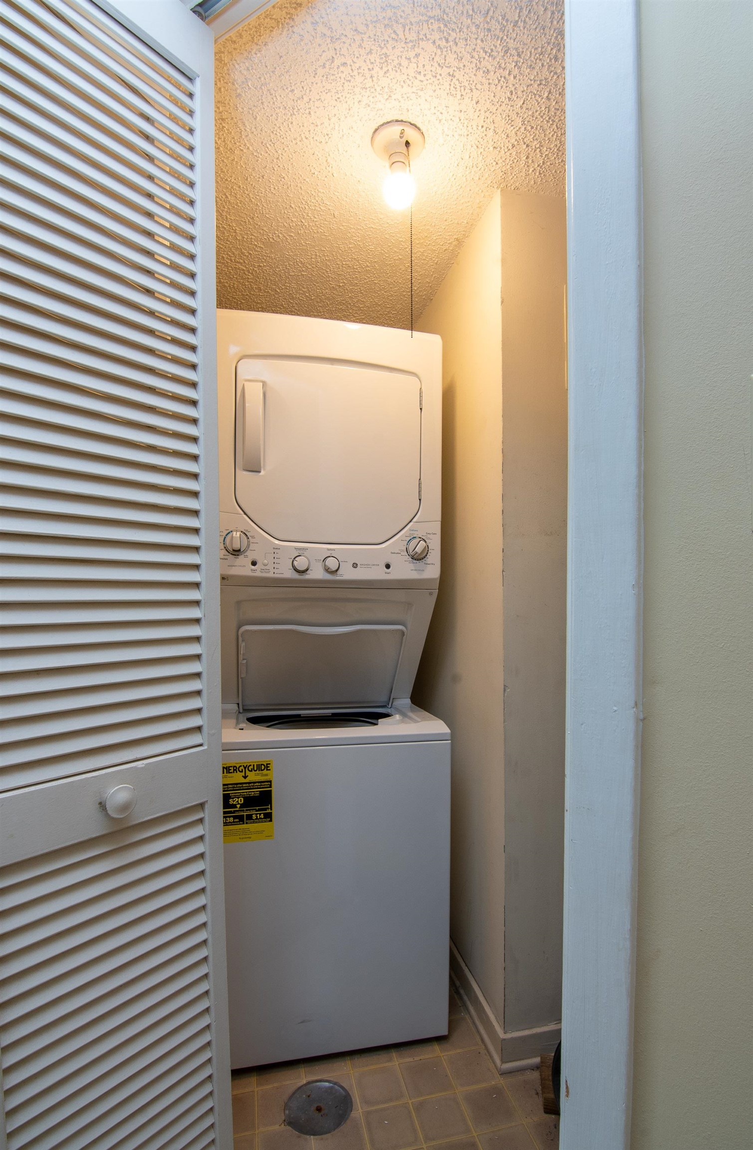 Laundry closet with a stacked washer and dryer behind a louvered door.