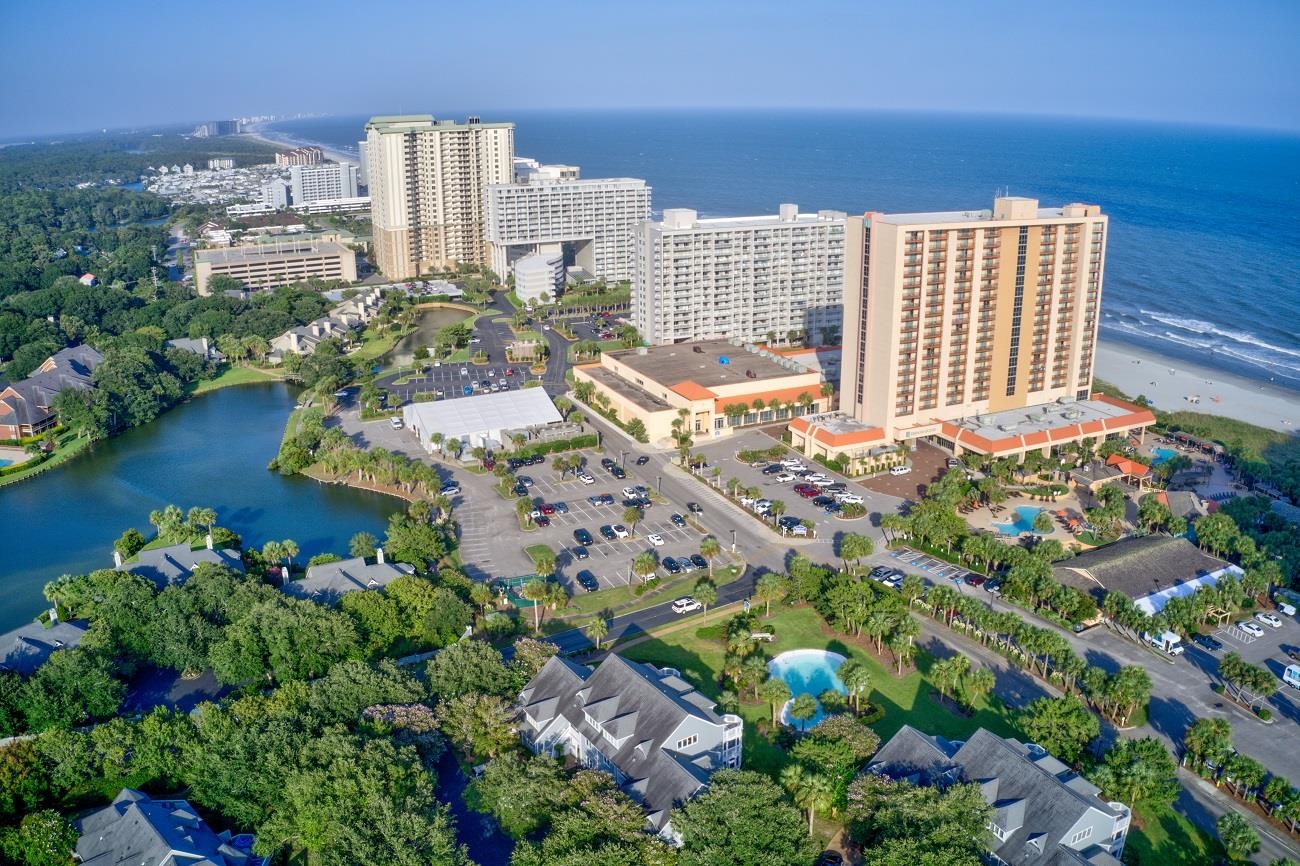 Aerial view of beachfront condominium towers beside the ocean, with a lagoon and pools nearby.