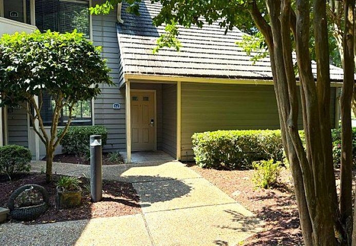 Townhome entrance with a shaded walkway, attached garage, and mature landscaping.