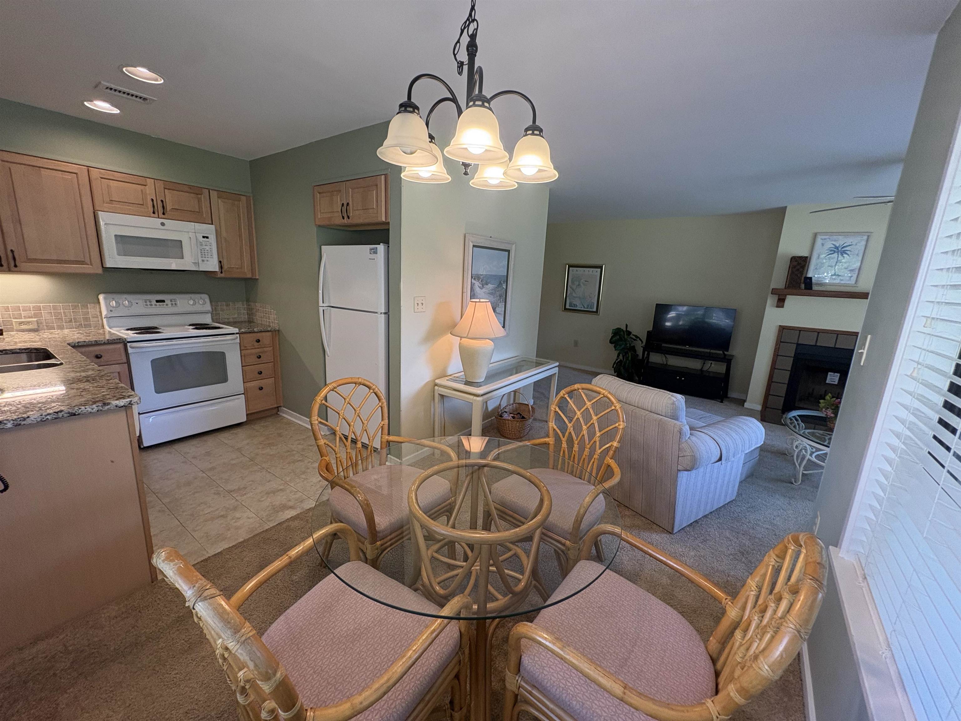Open-plan kitchen, dining, and living area with a glass dining table and wicker chairs.