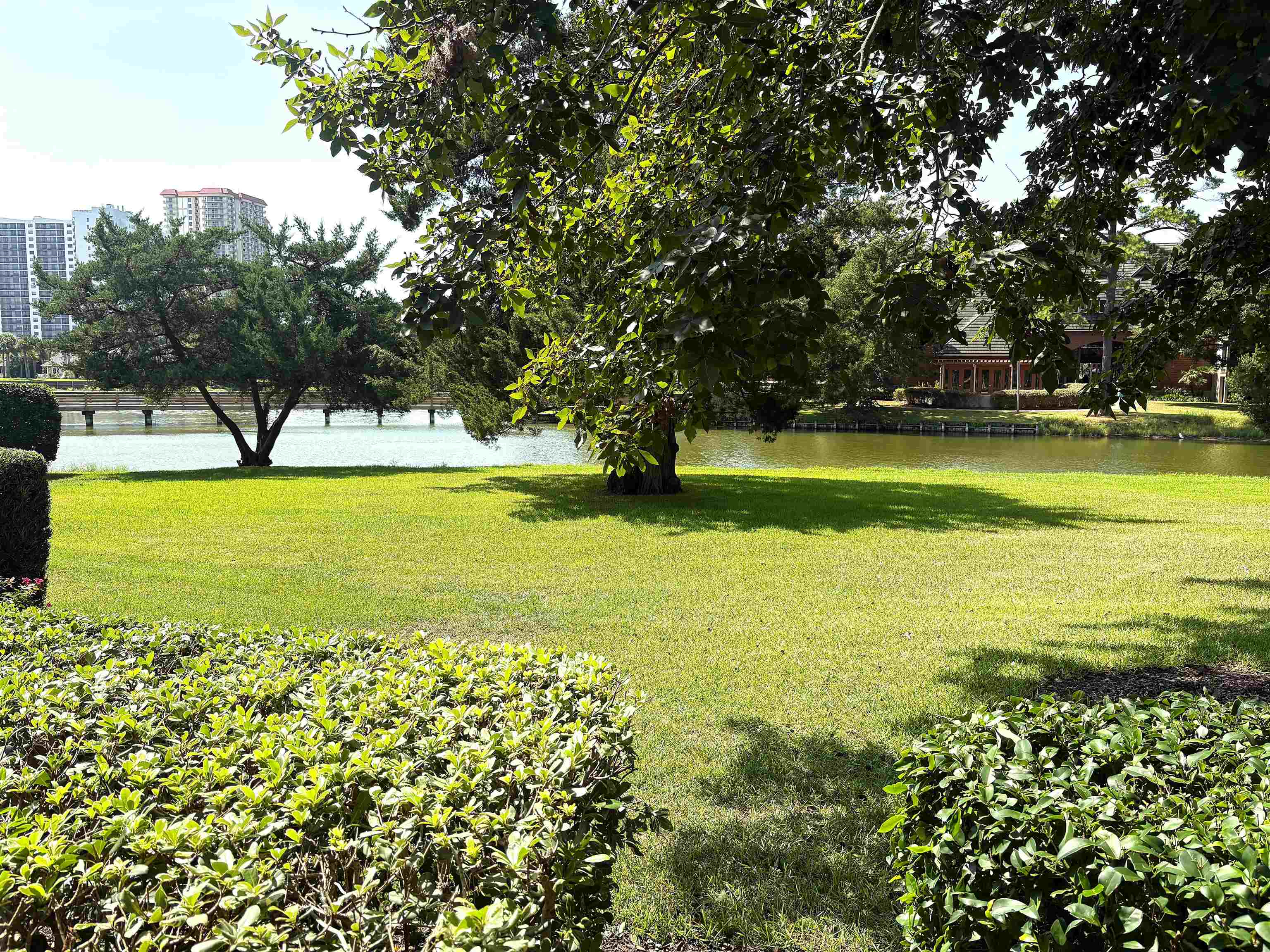 Landscaped grounds beside a pond, with mature trees and buildings across the water.