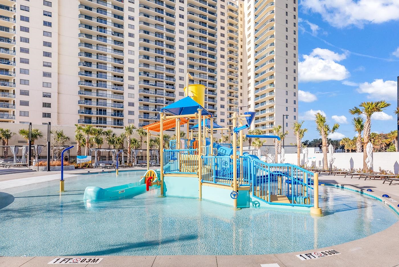 Condominium pool with a colorful children’s water-play structure and high-rise building behind it.
