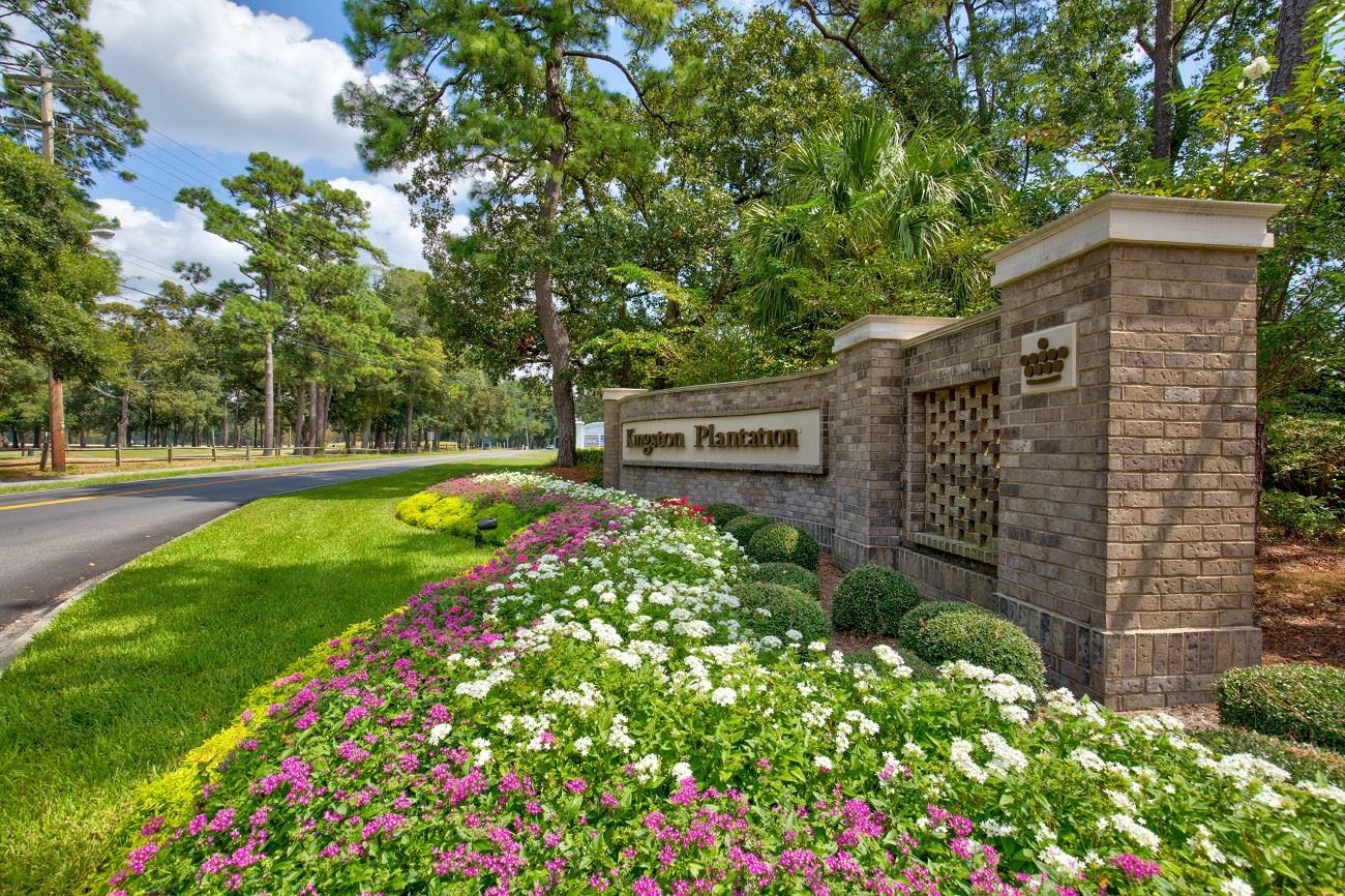 Kingston Plantation entrance sign beside a flower garden and tree-lined road.