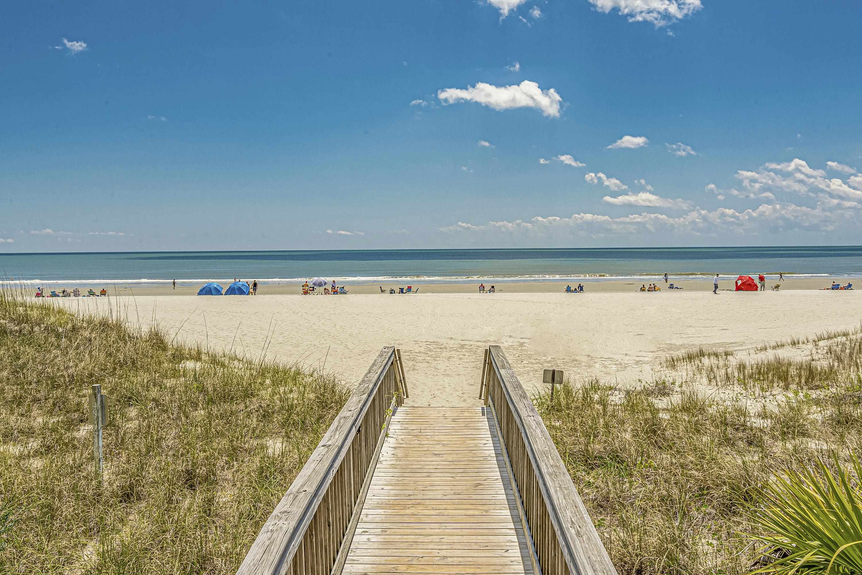 Beach access boardwalk leading through dunes to a sandy beach and ocean.