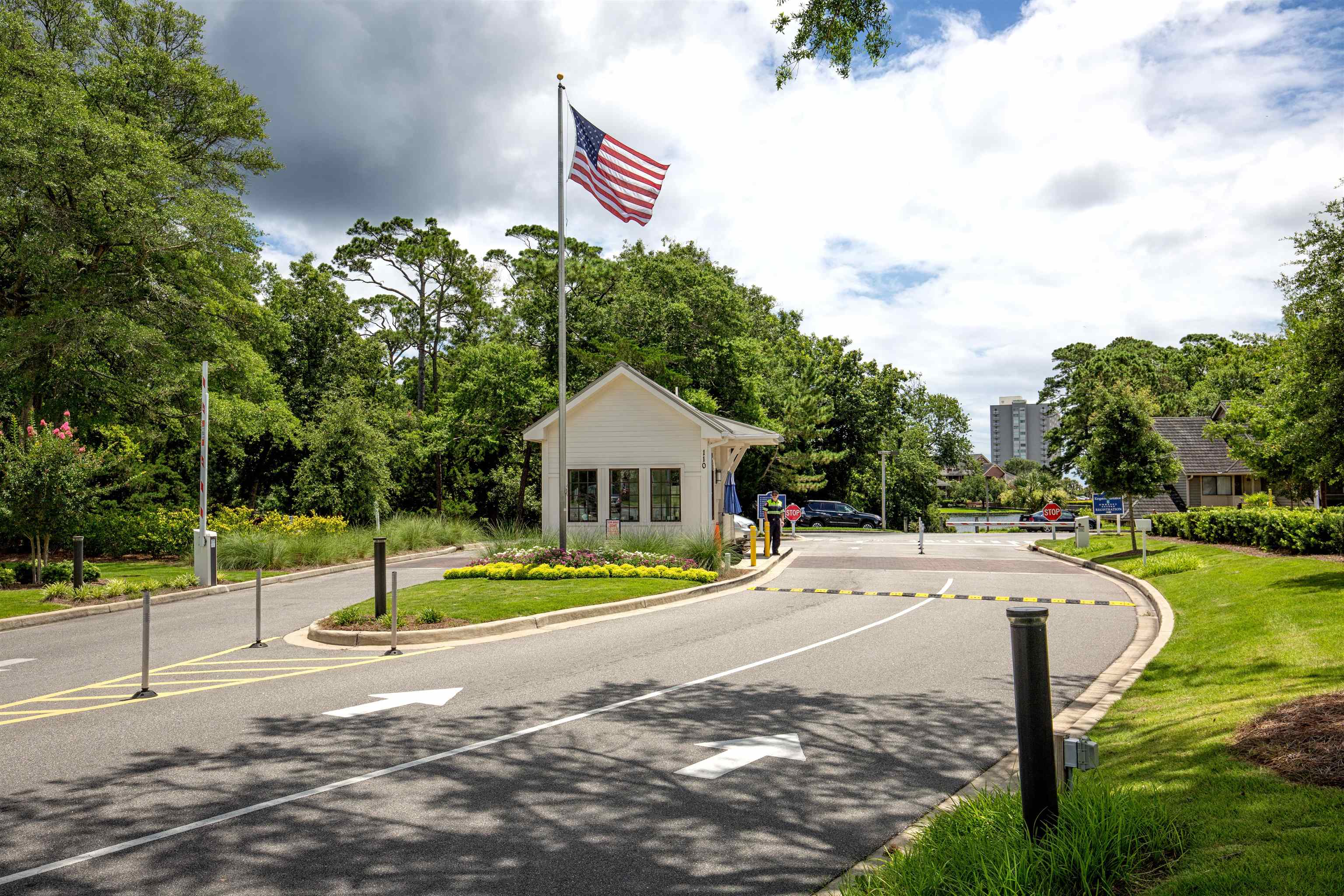 Gated community entrance with a guard booth, landscaped grounds, and a large American flag.