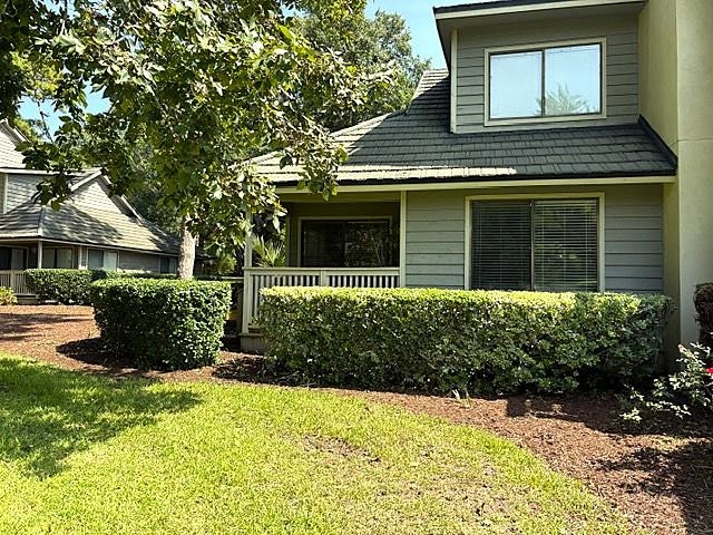 Condominium exterior with a covered porch, dormer window, and trimmed hedges.