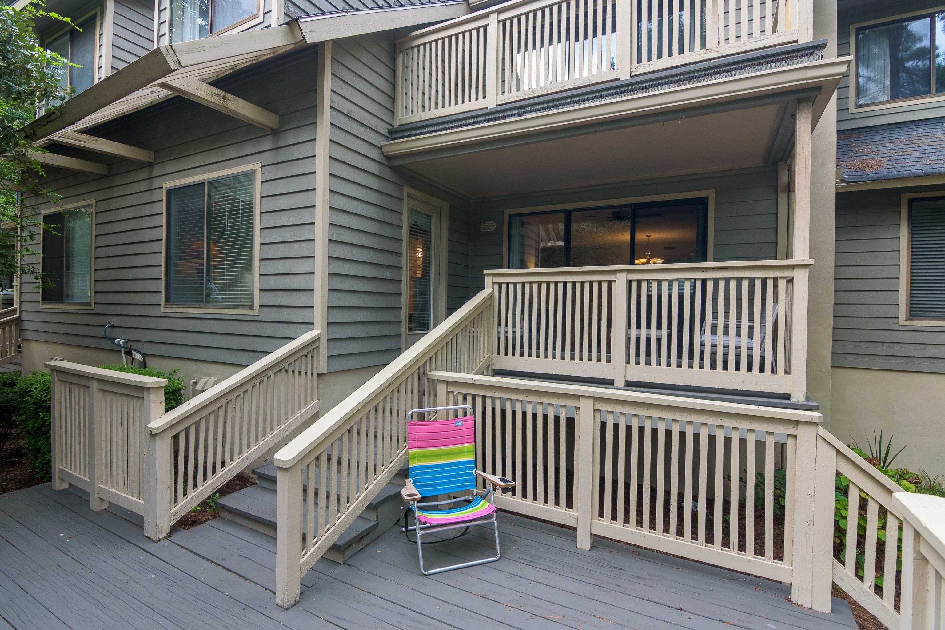 Condominium exterior with raised deck, wooden stairs, and a colorful folding chair.