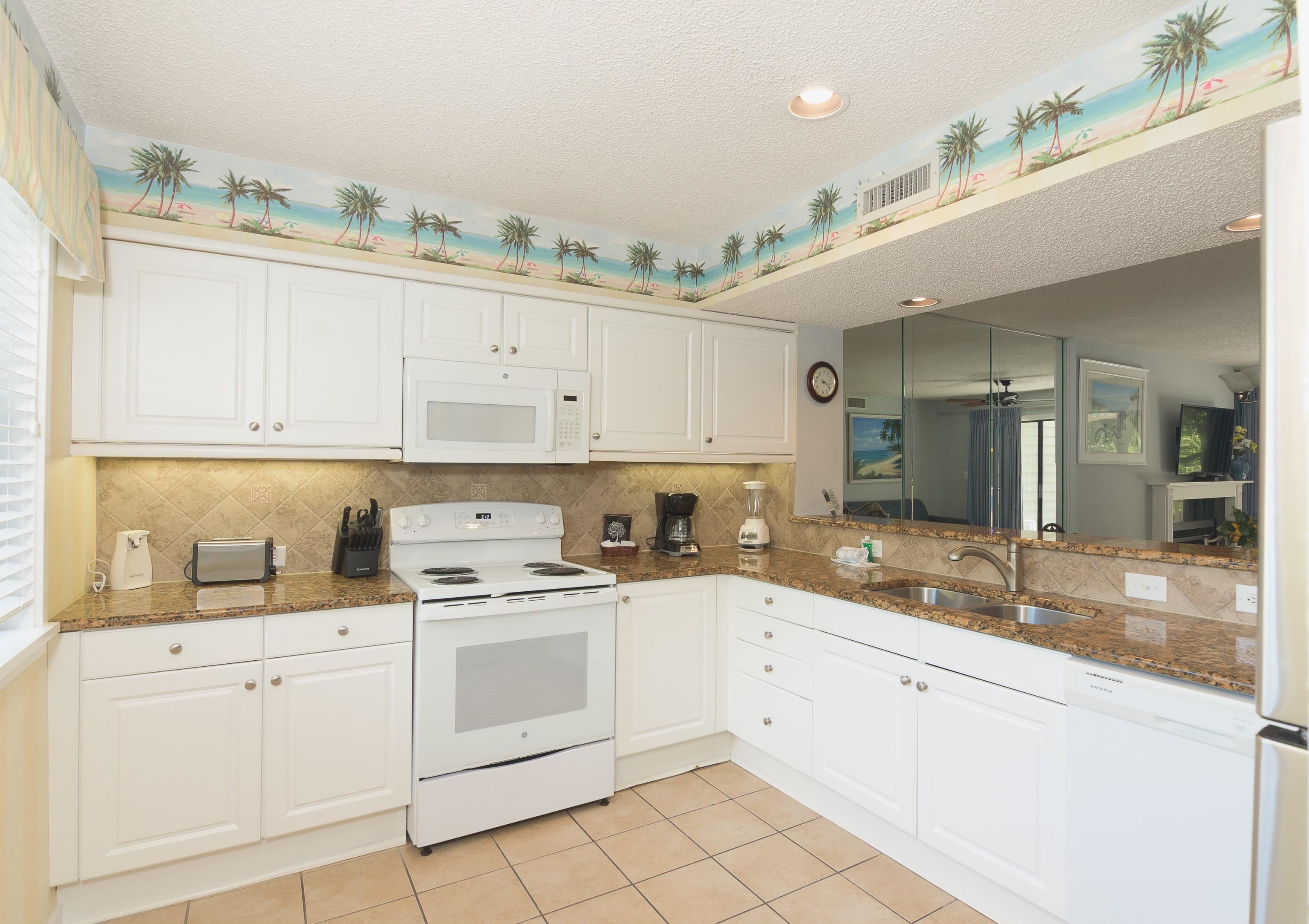 Kitchen with white cabinets, granite counters, and a tropical beach wallpaper border.