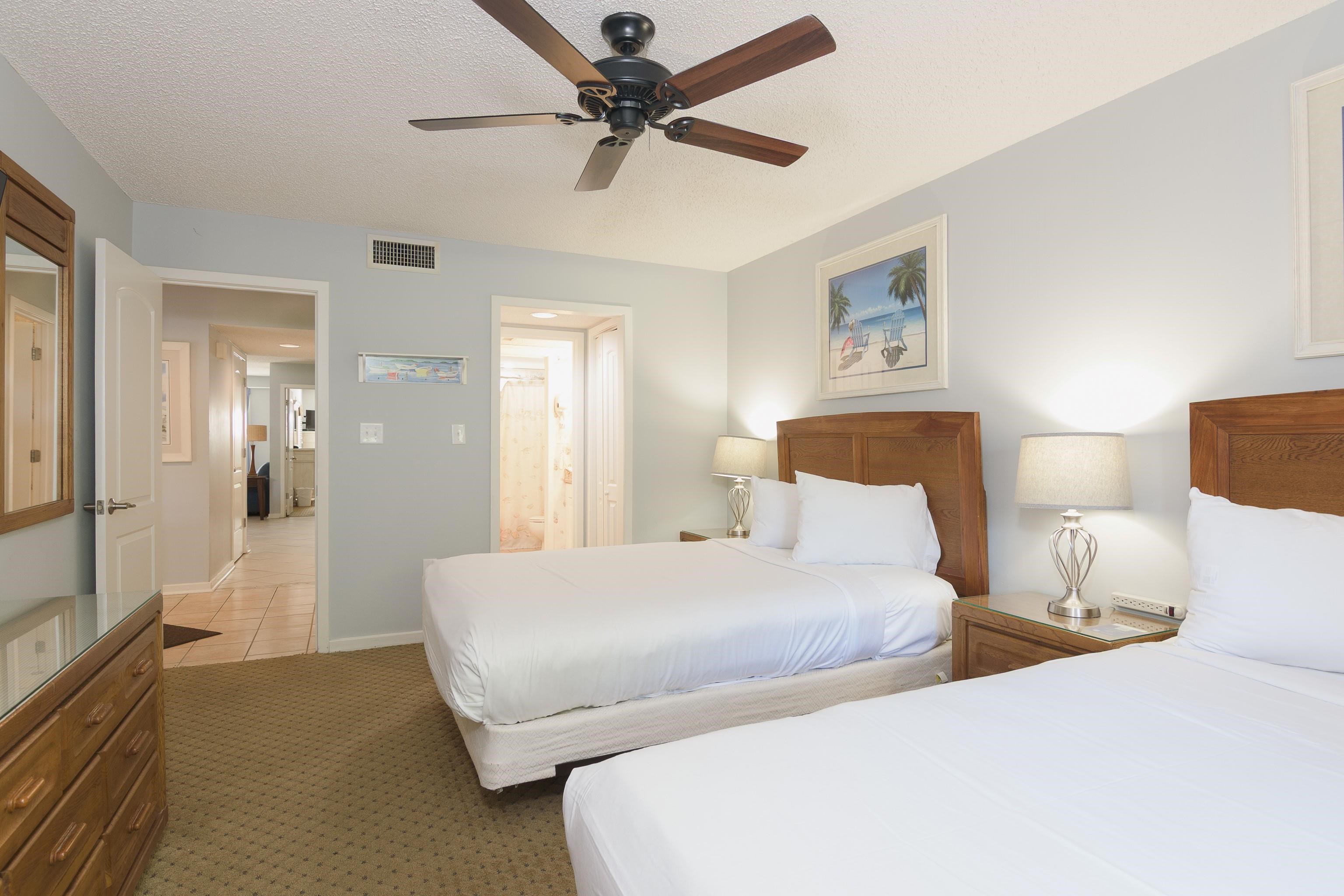 Bedroom with two white beds, wood furniture, bedside lamps, and a ceiling fan.