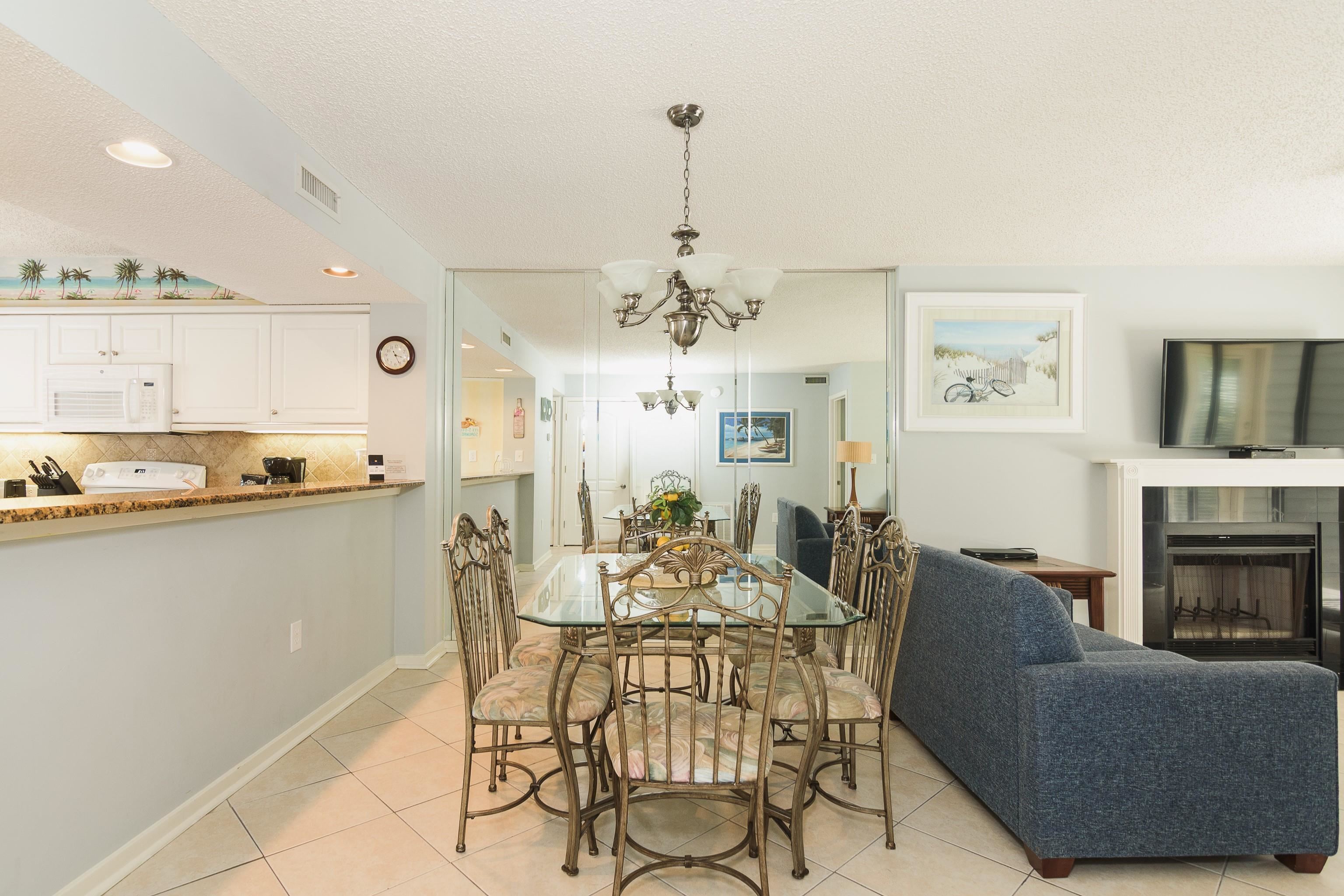 Furnished condo dining and living area with a mirrored wall, blue sofa, and fireplace.