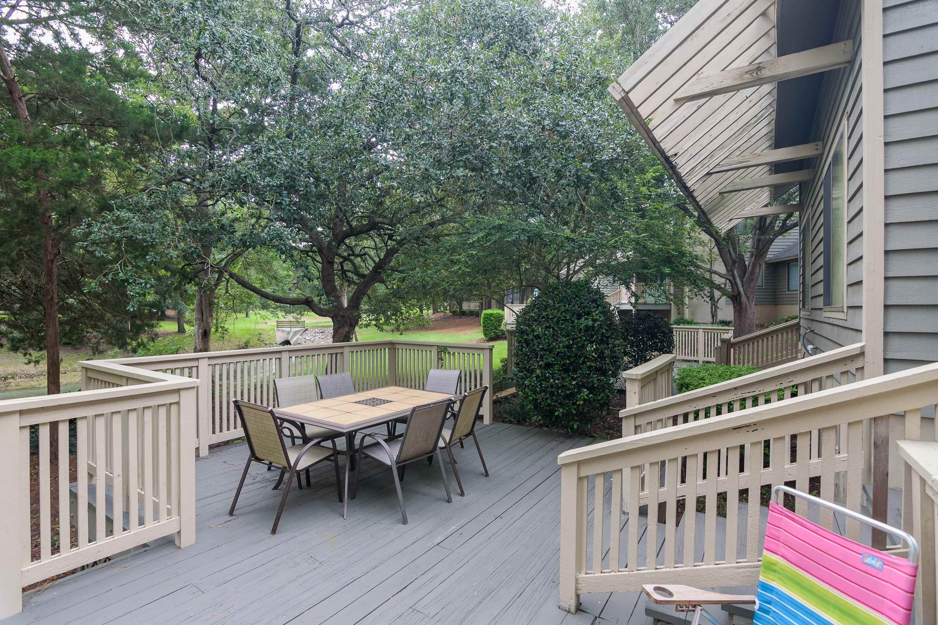 Townhouse deck with outdoor dining set, beige railings, and mature trees.